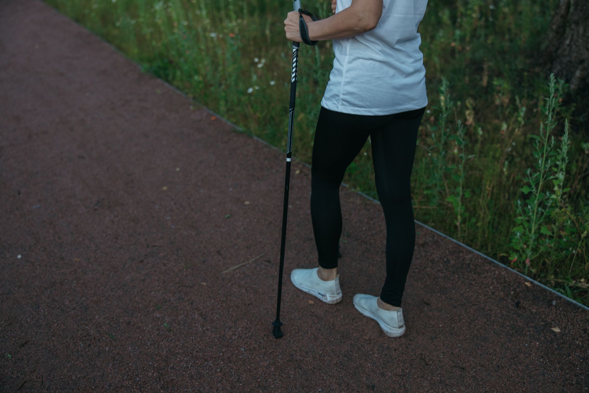 Individual using a walking pole, practicing mobility on a pathway surrounded by greenery.