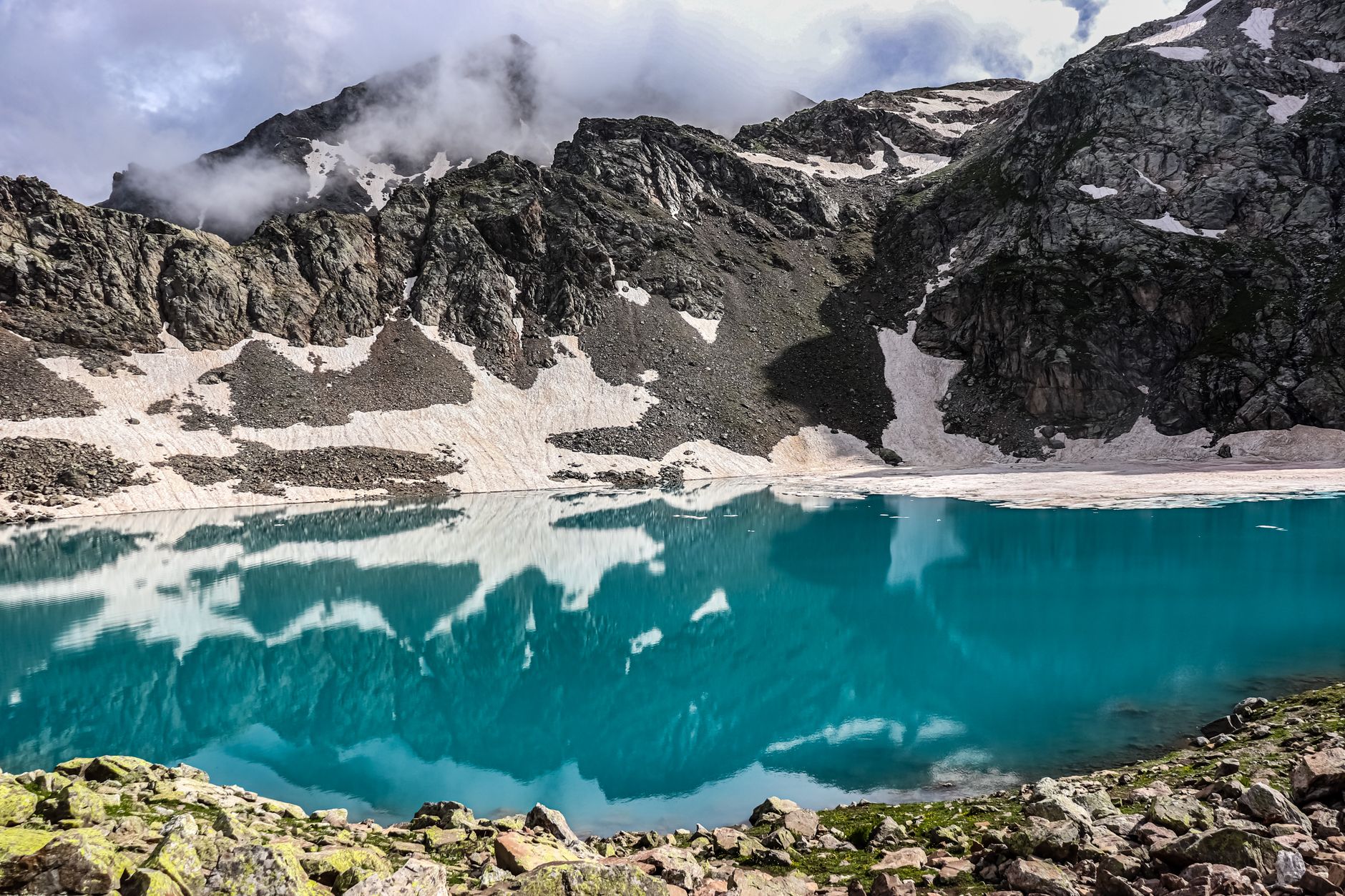 A stunning glacial lake reflecting surrounding mountains and clouds.