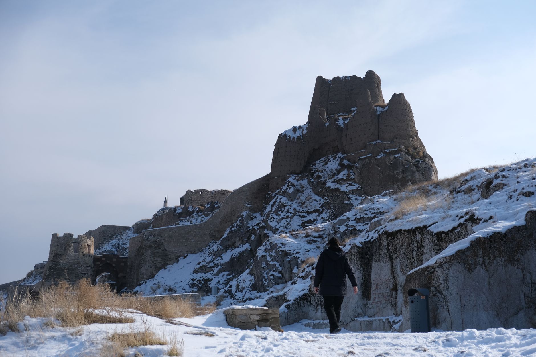 A person walking towards the snow-covered Van Castle perched on a hill.