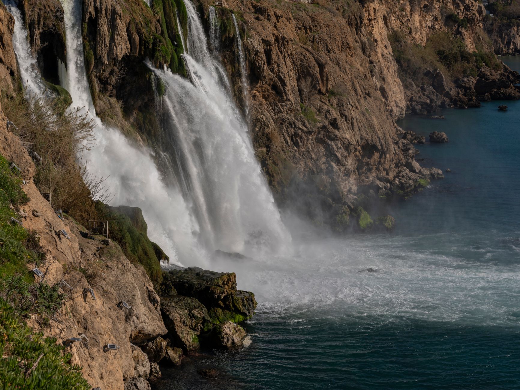 A majestic waterfall plunges off a rocky cliff into the Mediterranean Sea.