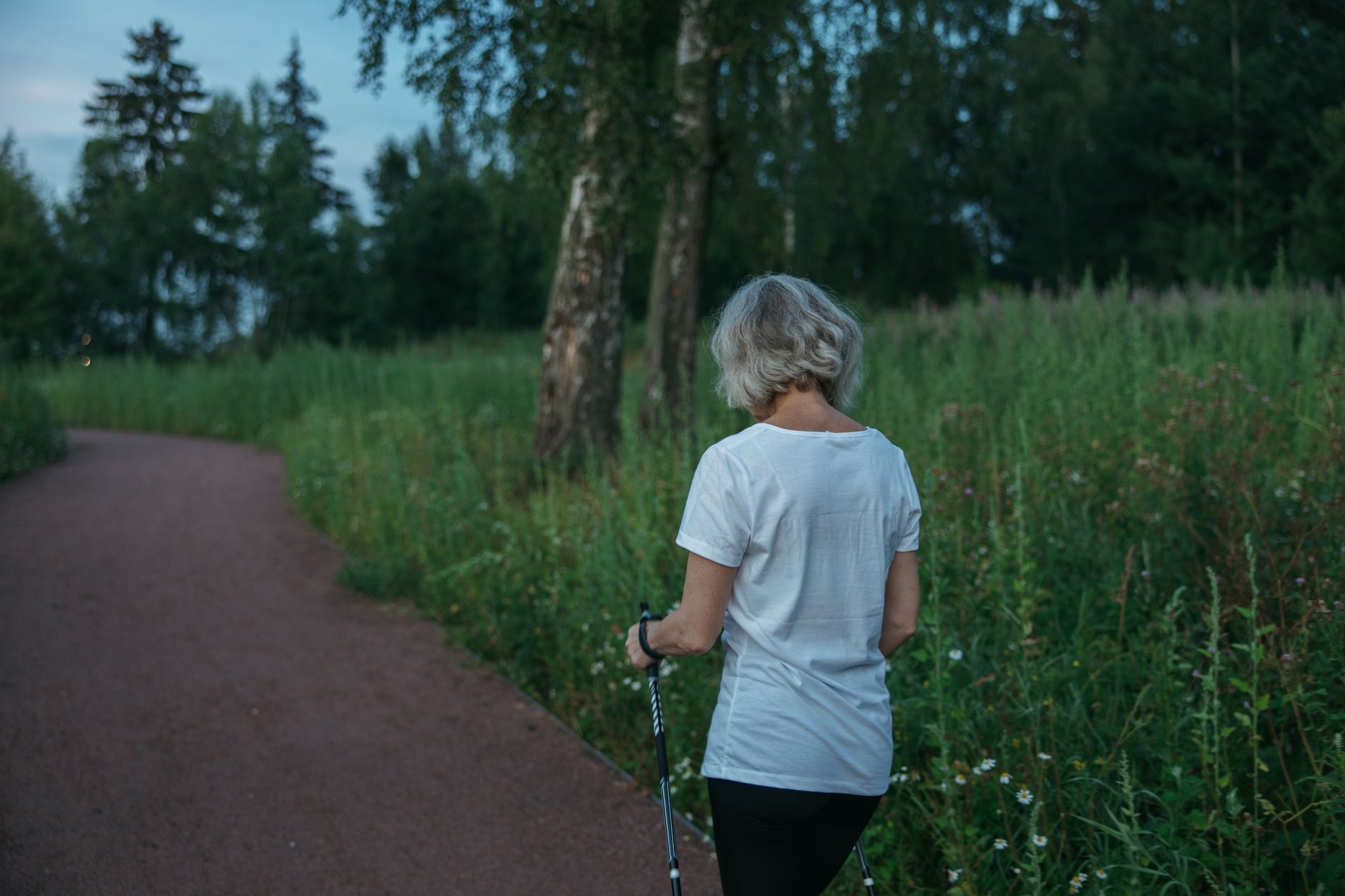 An older woman walks peacefully on a path in a green park.