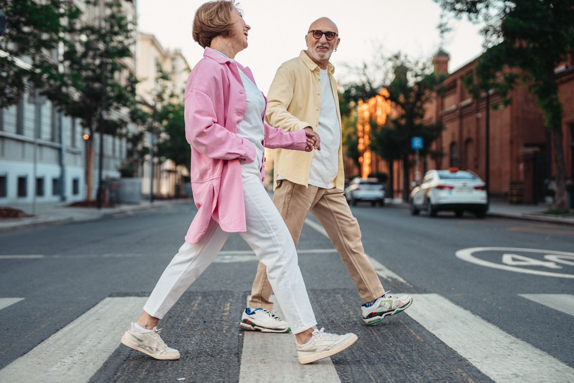 An elderly couple happily crossing the street in casual attire.