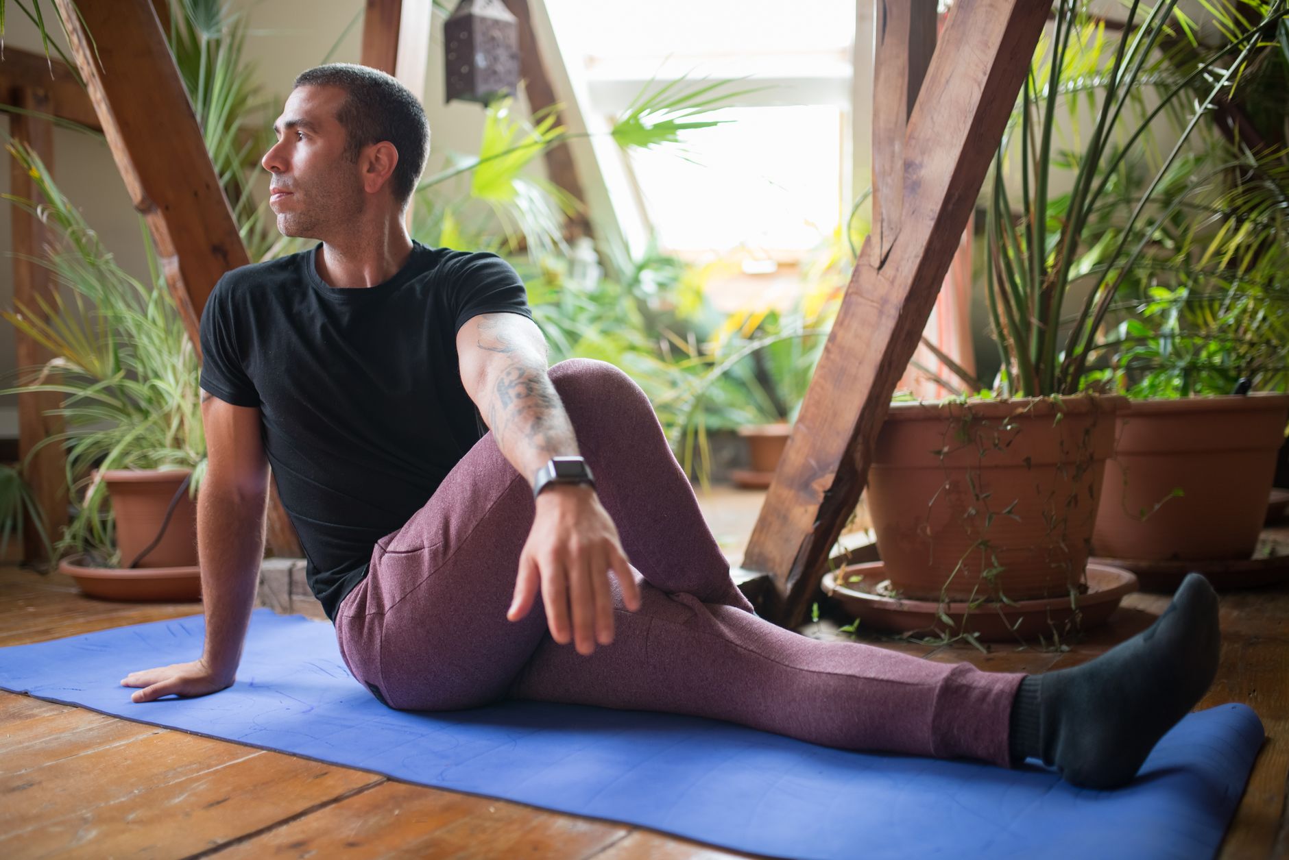 Man performing exercises on a yoga mat at home, surrounded by plants.