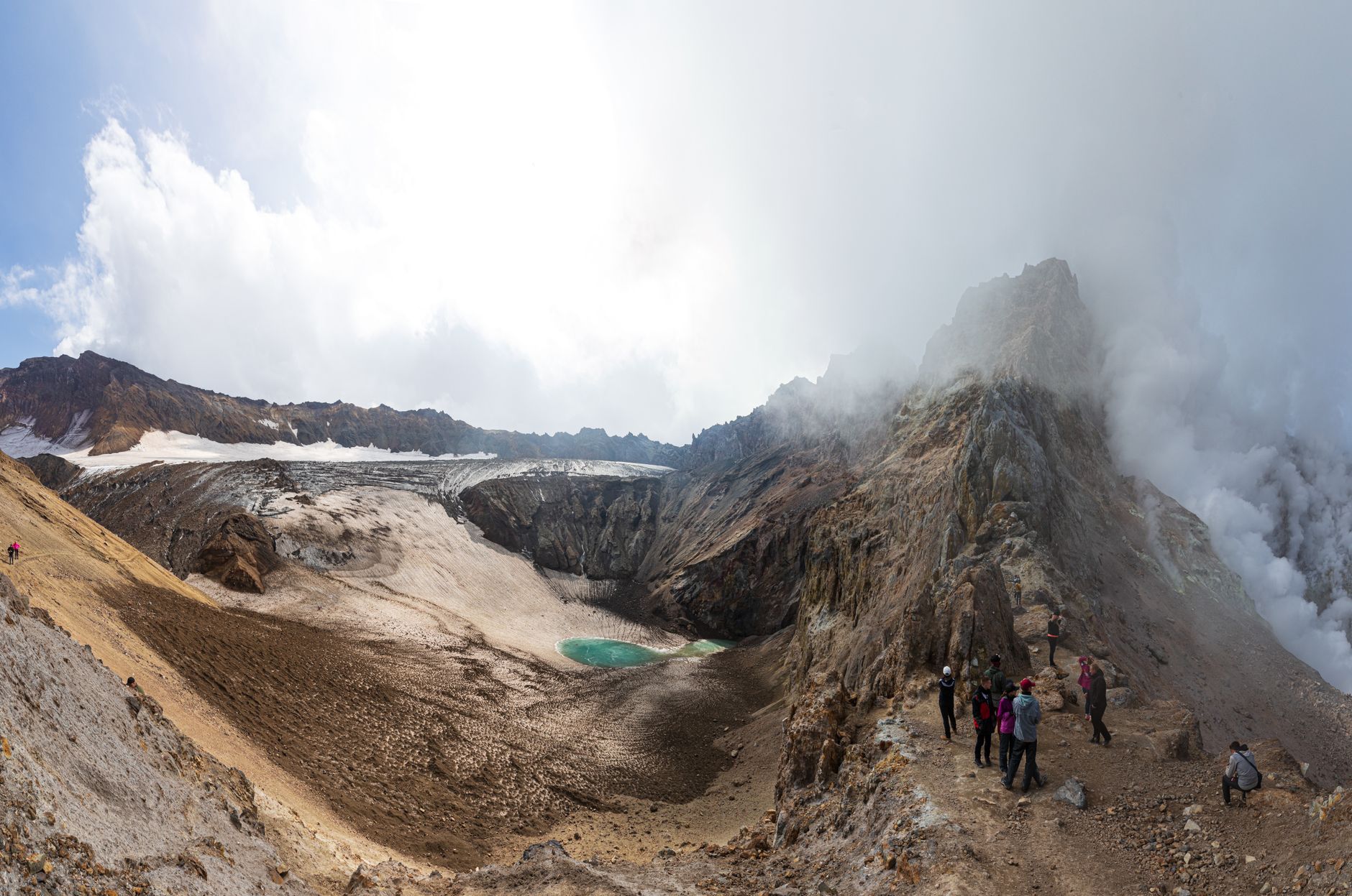徒步者在火山口边缘附近的火山步道上，背景是一座冰川湖。