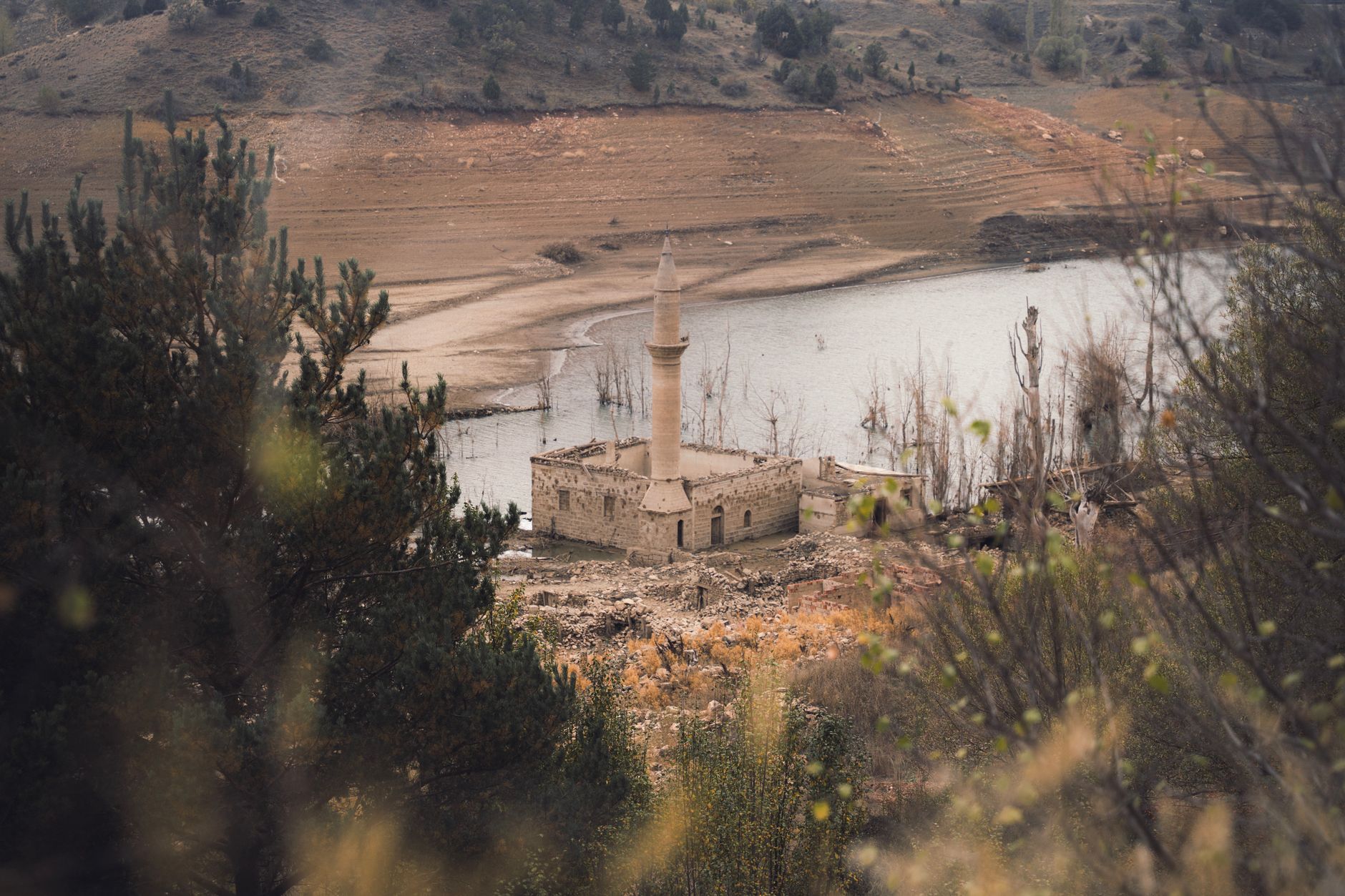 Partially submerged ancient mosque ruins at Lake Bafa, surrounded by trees.