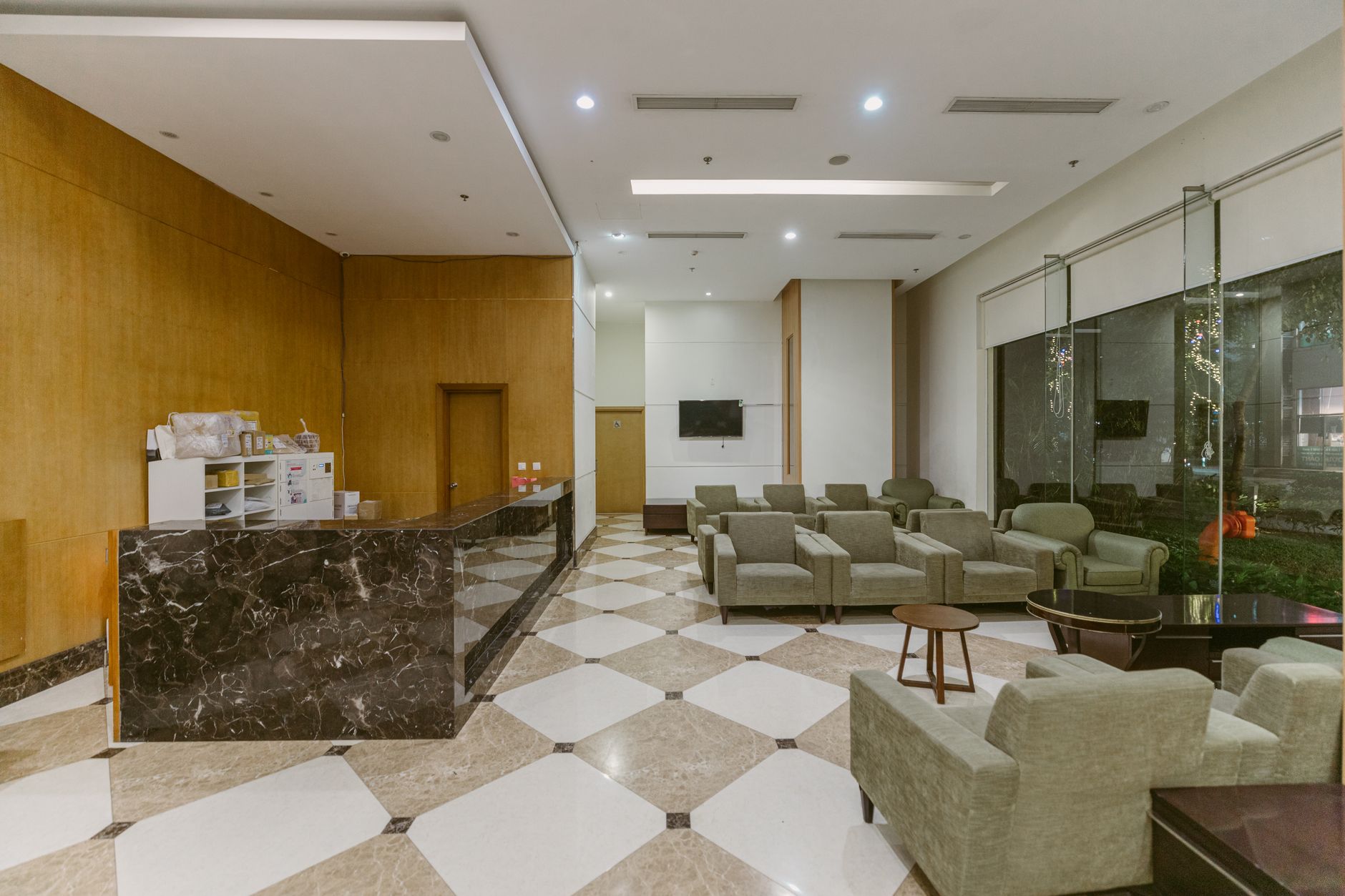 Spacious hospital lounge with green chairs and a reception desk.