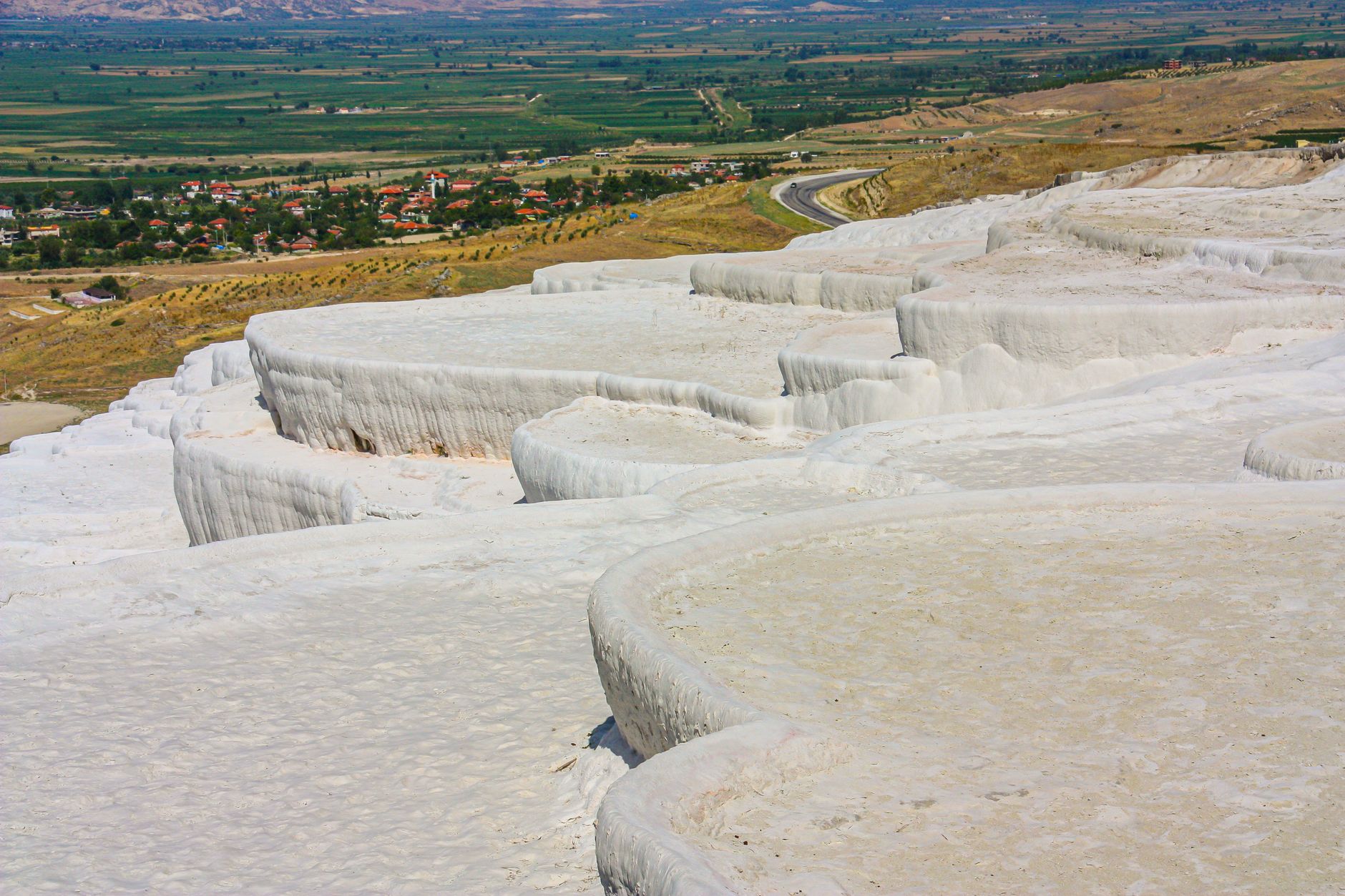 View of Pamukkale's white travertine terraces with lush fields and distant Laodikeia.