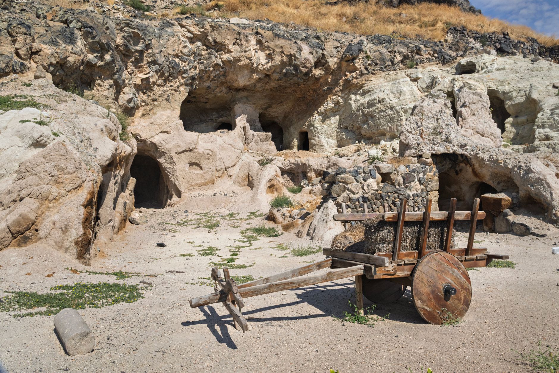 Kaklık Cave featuring rock formations and a wooden cart in sandy terrain.