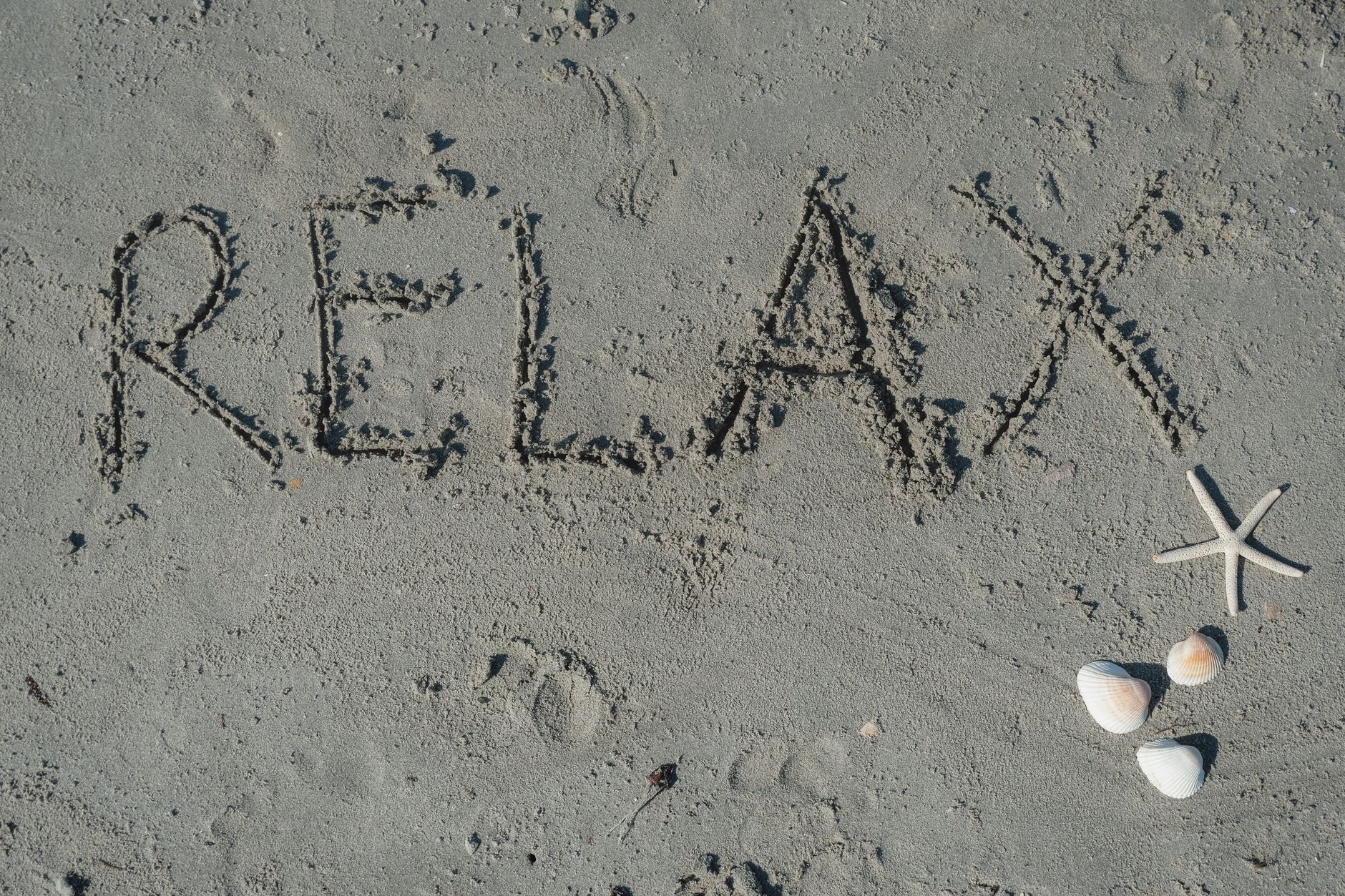 The word 'RELAX' is written in sand, accompanied by seashells and a starfish.