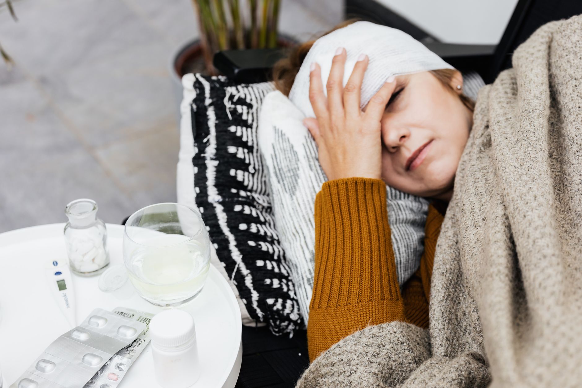 A woman resting at home with a headache, wrapped in a blanket.
