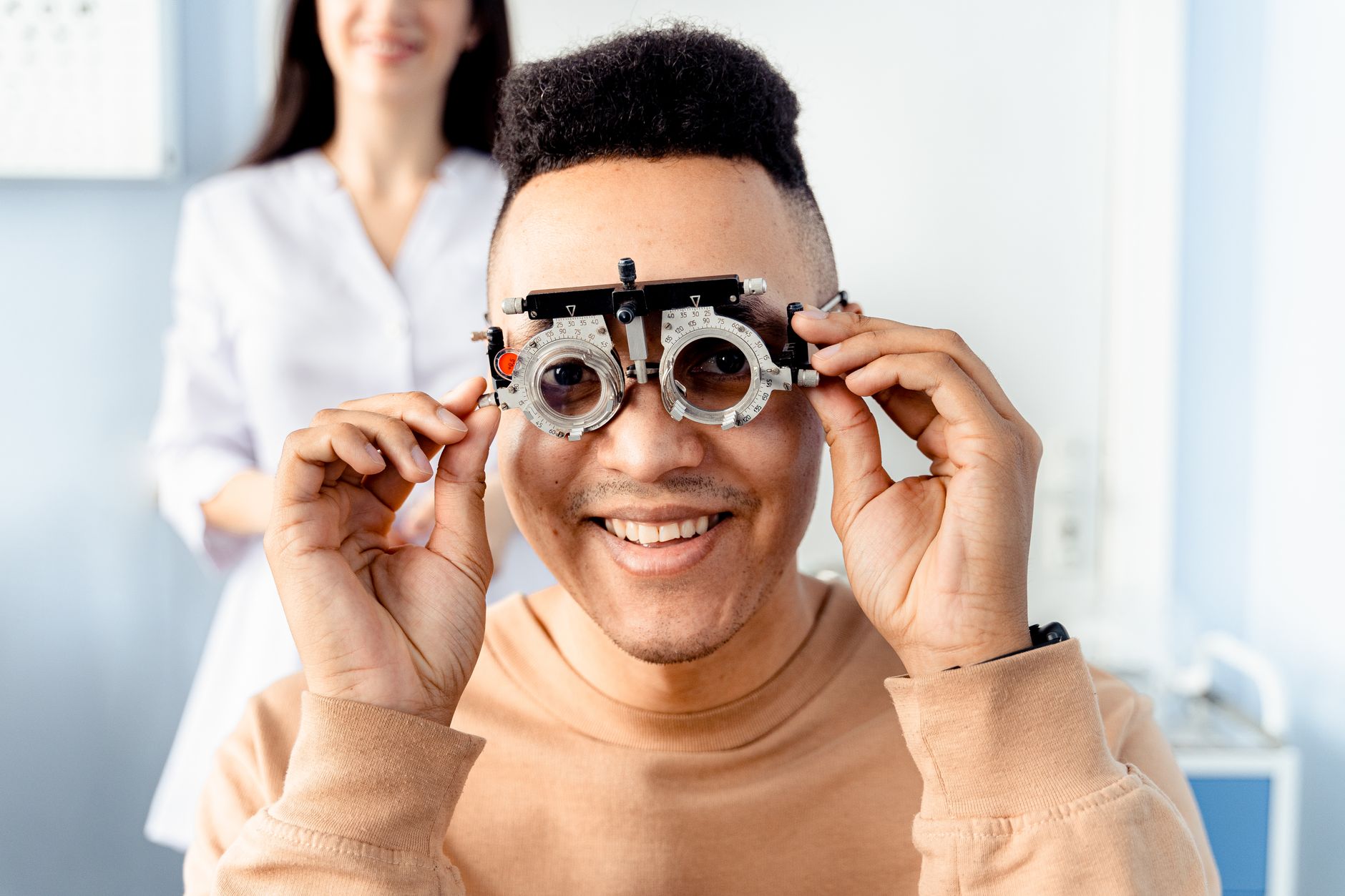 A smiling patient trying on vision correction glasses in an optometry clinic.