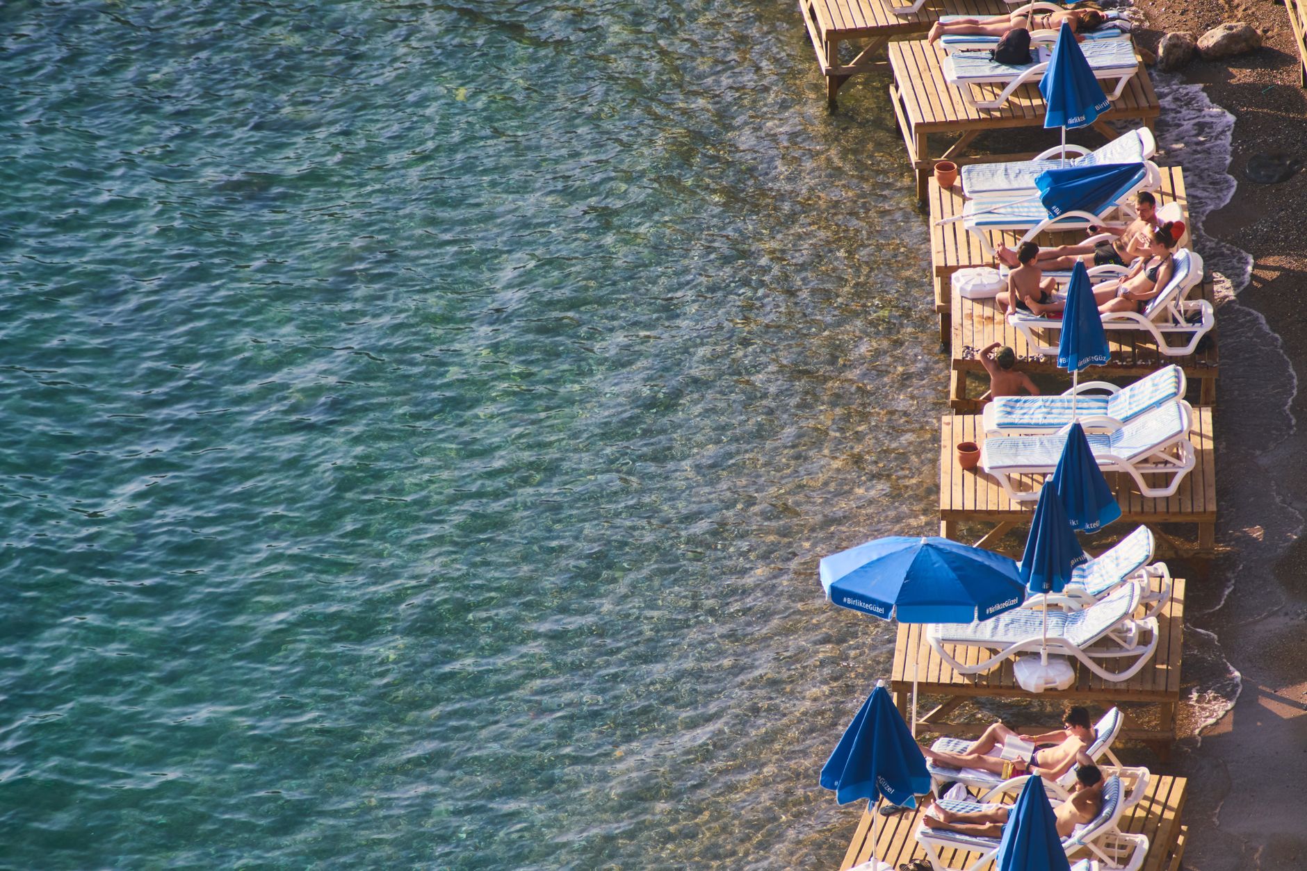View of sun loungers with umbrellas along the clear water of the Turkish Riviera.