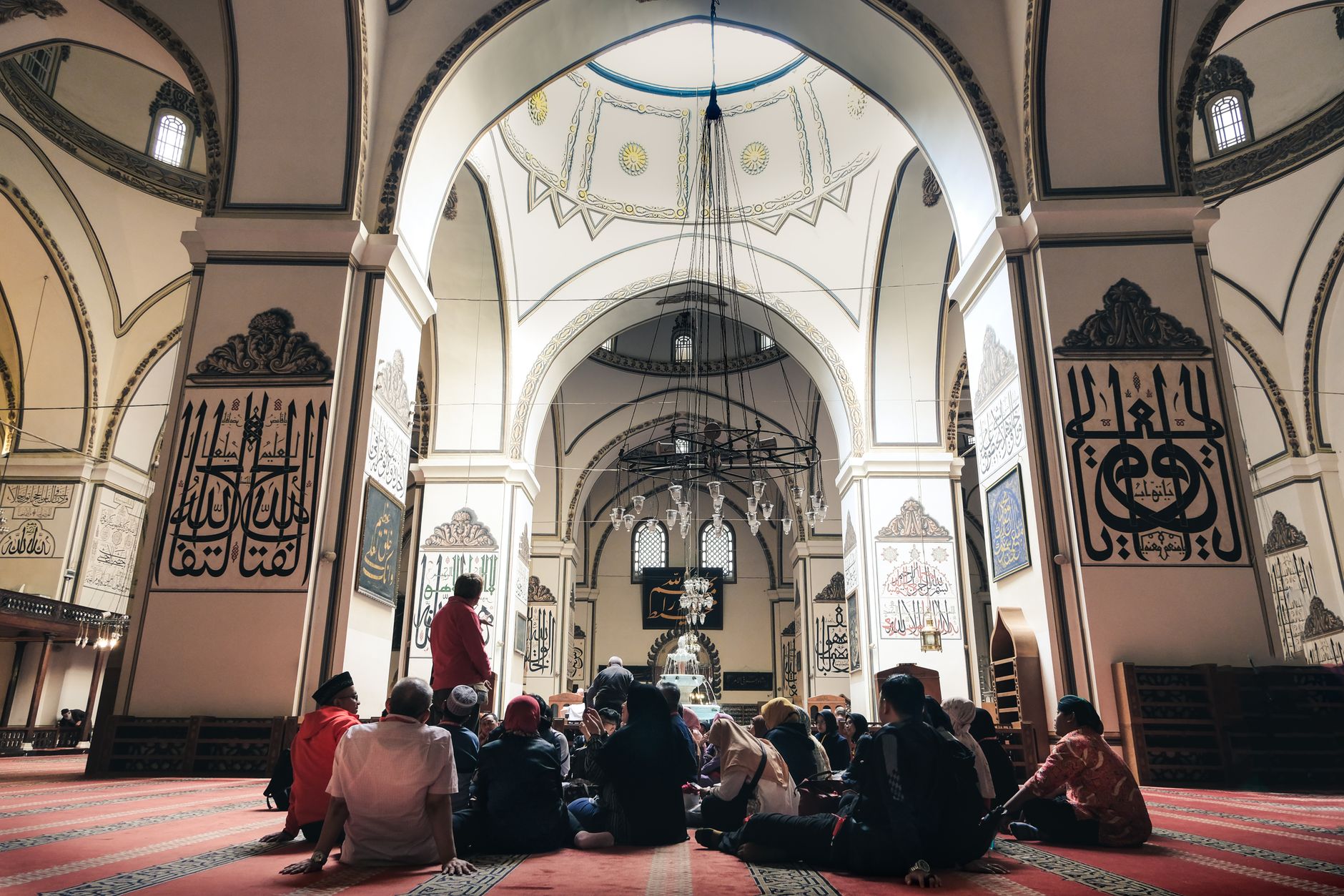 Visitors seated in the Grand Mosque of Bursa, surrounded by intricate calligraphy and architectural details.
