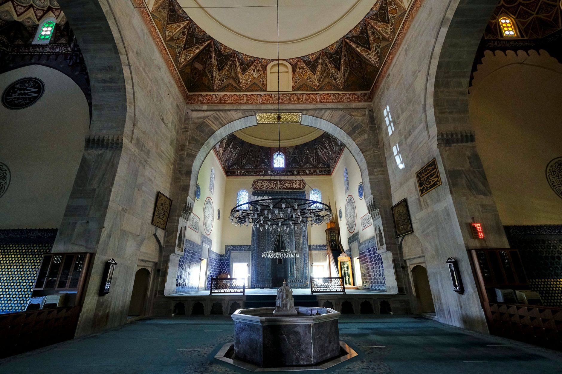 A stunning view of a mosque's interior featuring intricate patterns, colorful windows, and a central fountain.