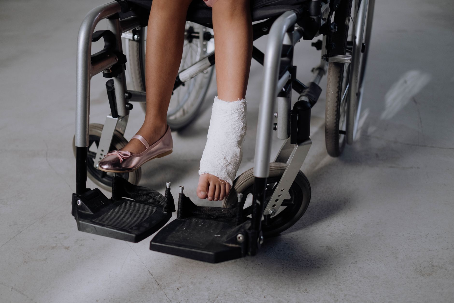 A young child in a wheelchair with a bandaged foot, wearing pink shoes.
