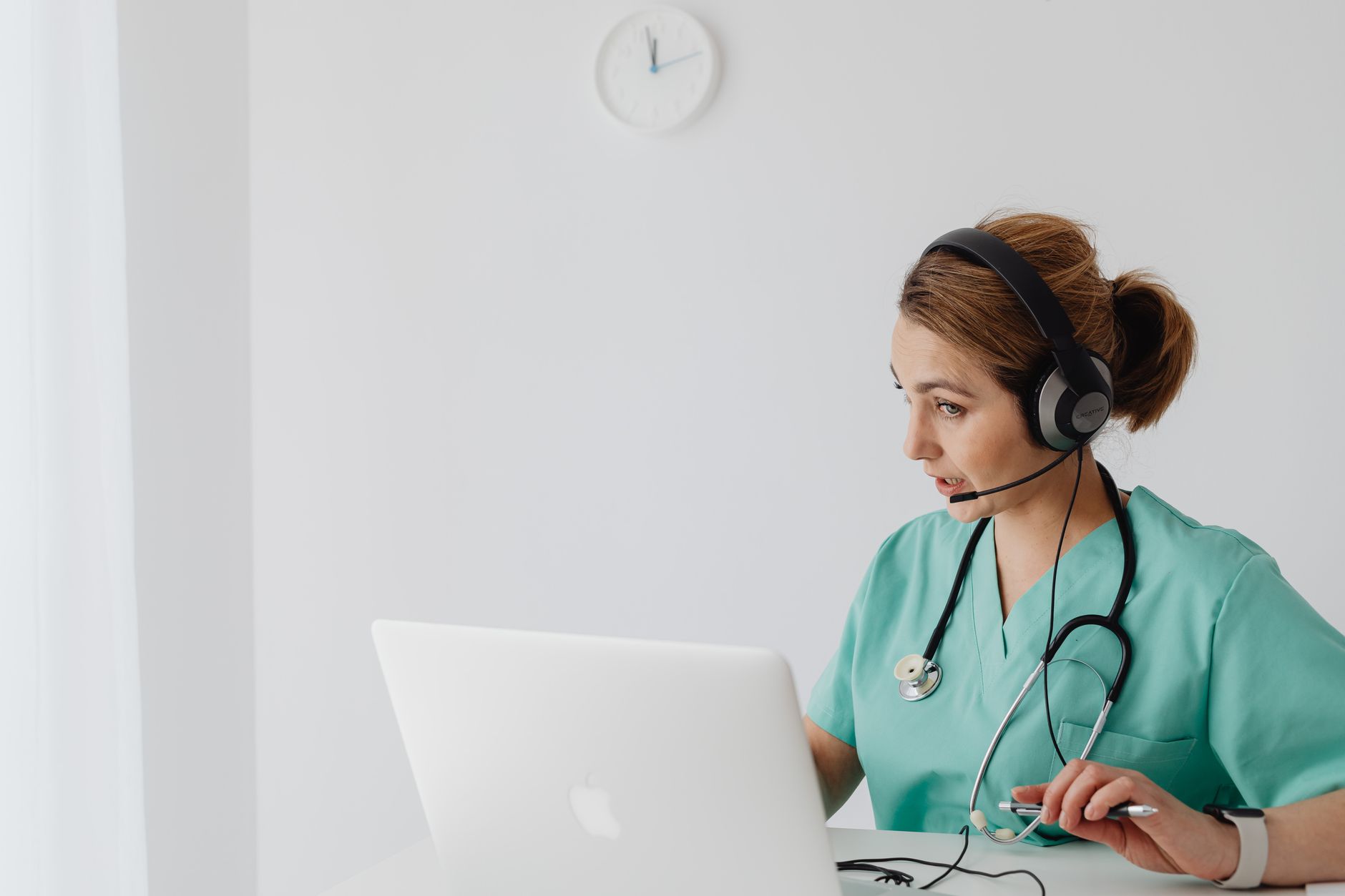 A doctor in green scrubs conducting a remote video call using a laptop.