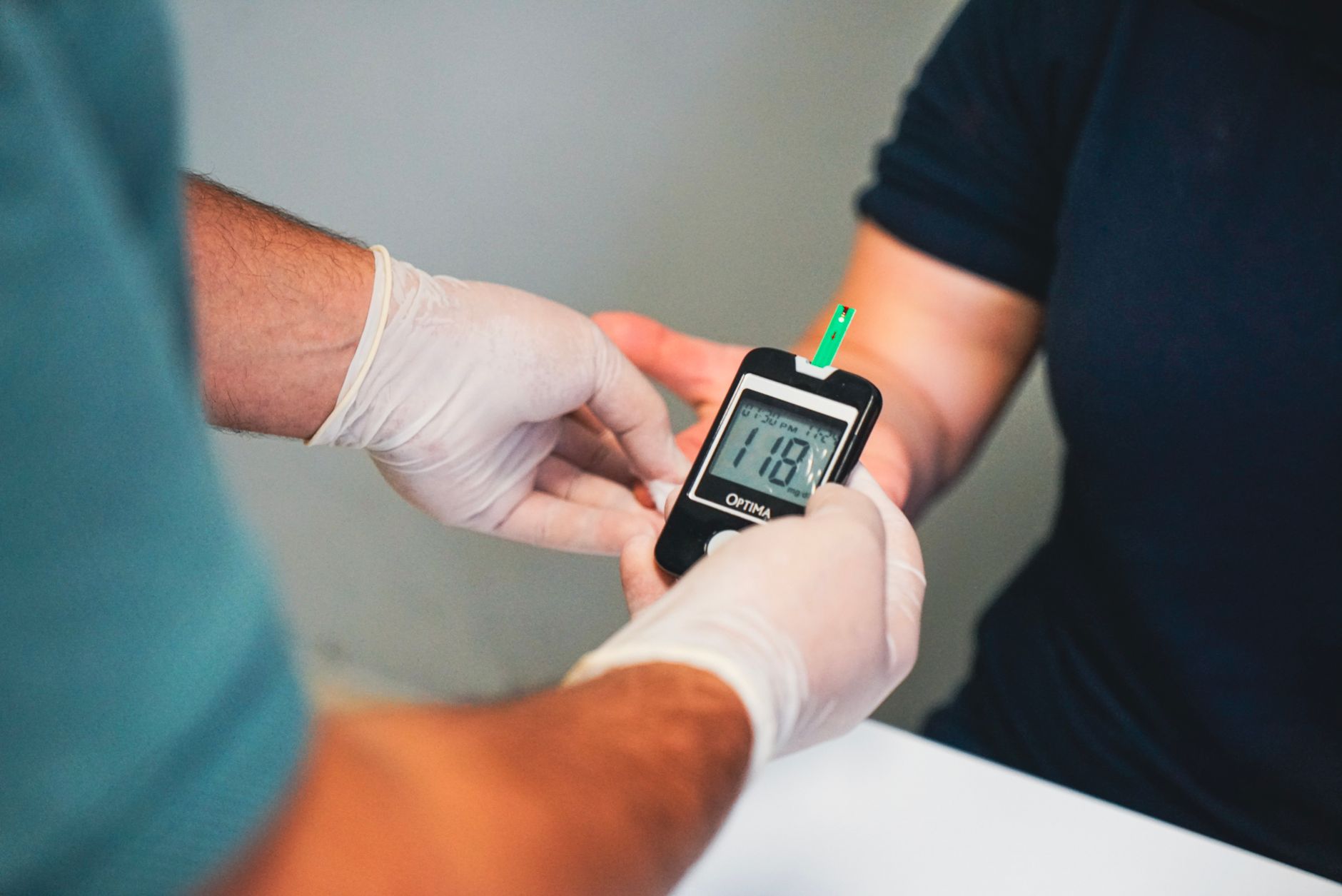 A nurse in gloves measures a patient's blood glucose level using a meter.