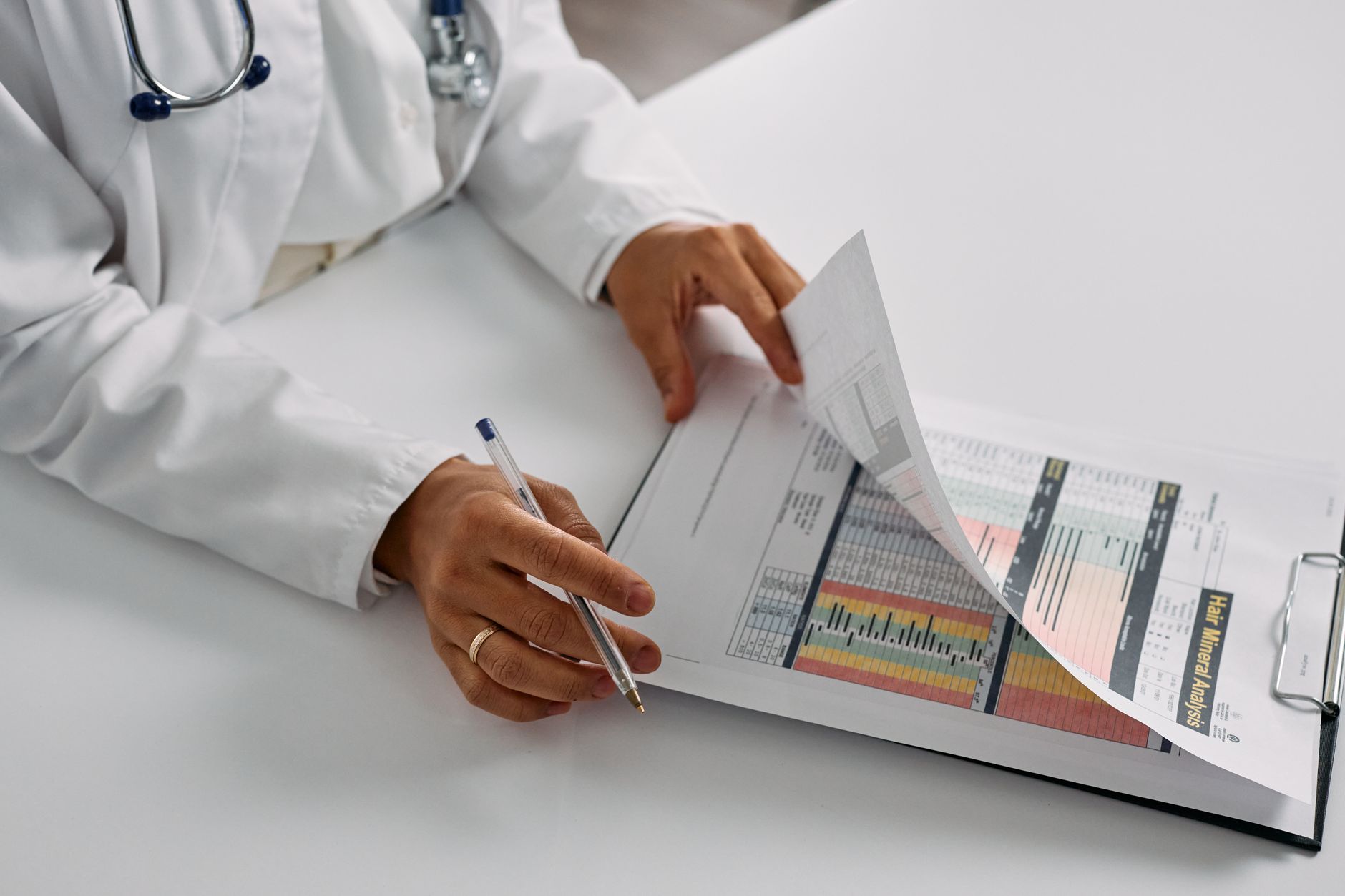 A Turkish doctor examines patient records with a pen in a bright consultation room.