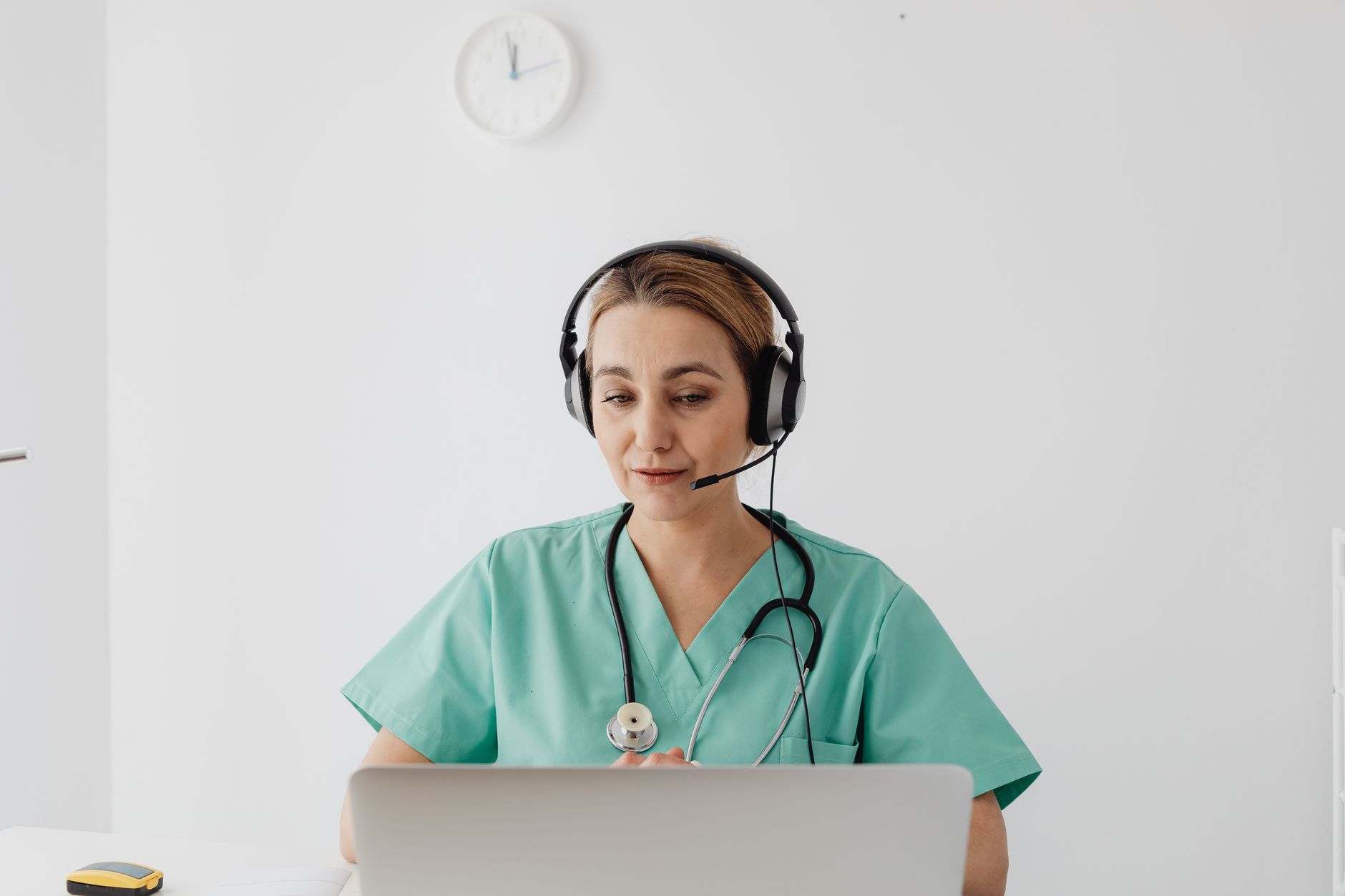 A healthcare professional in green scrubs engages in a virtual consultation using a laptop.