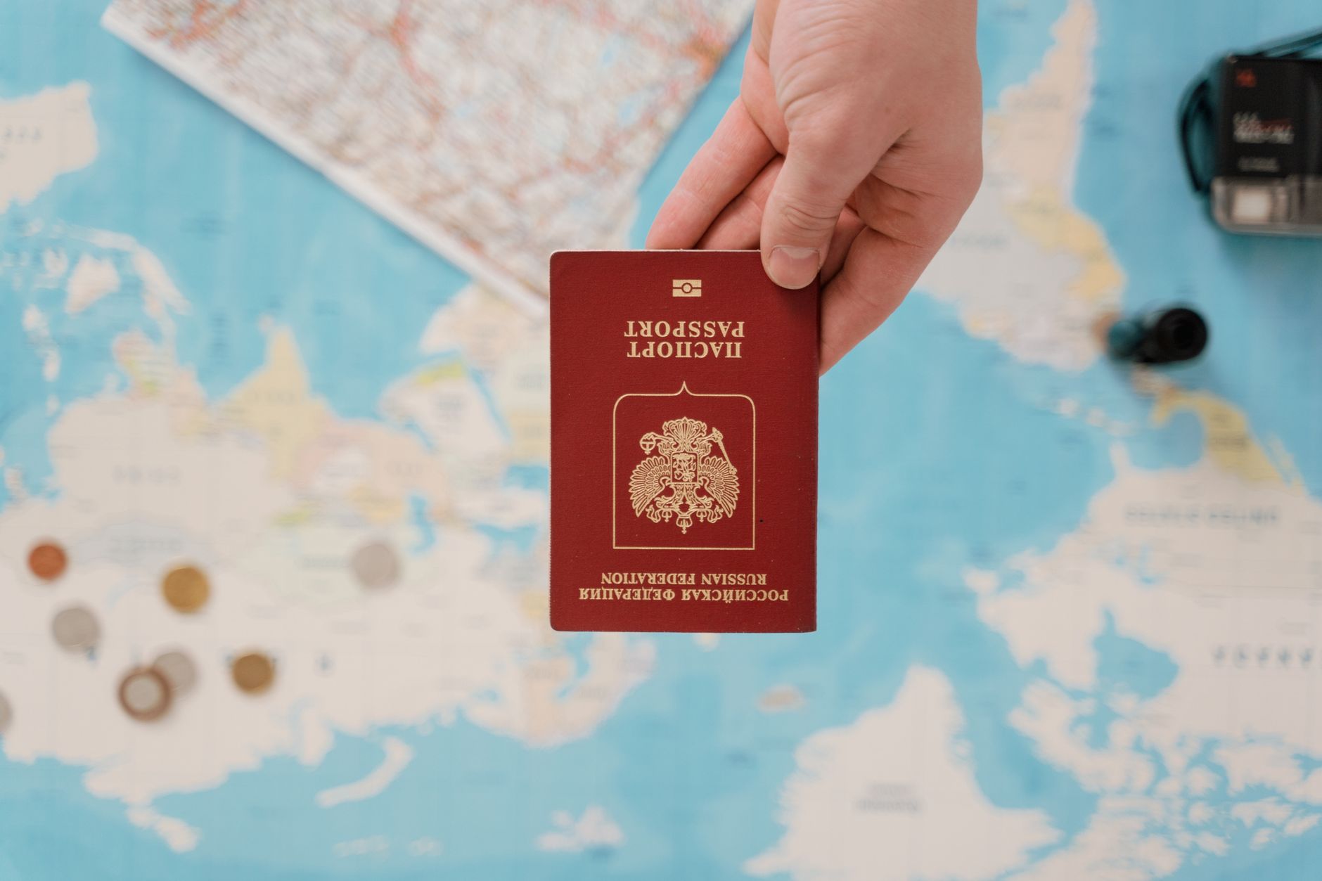 A hand holding a red passport above a map, symbolizing travel logistics.