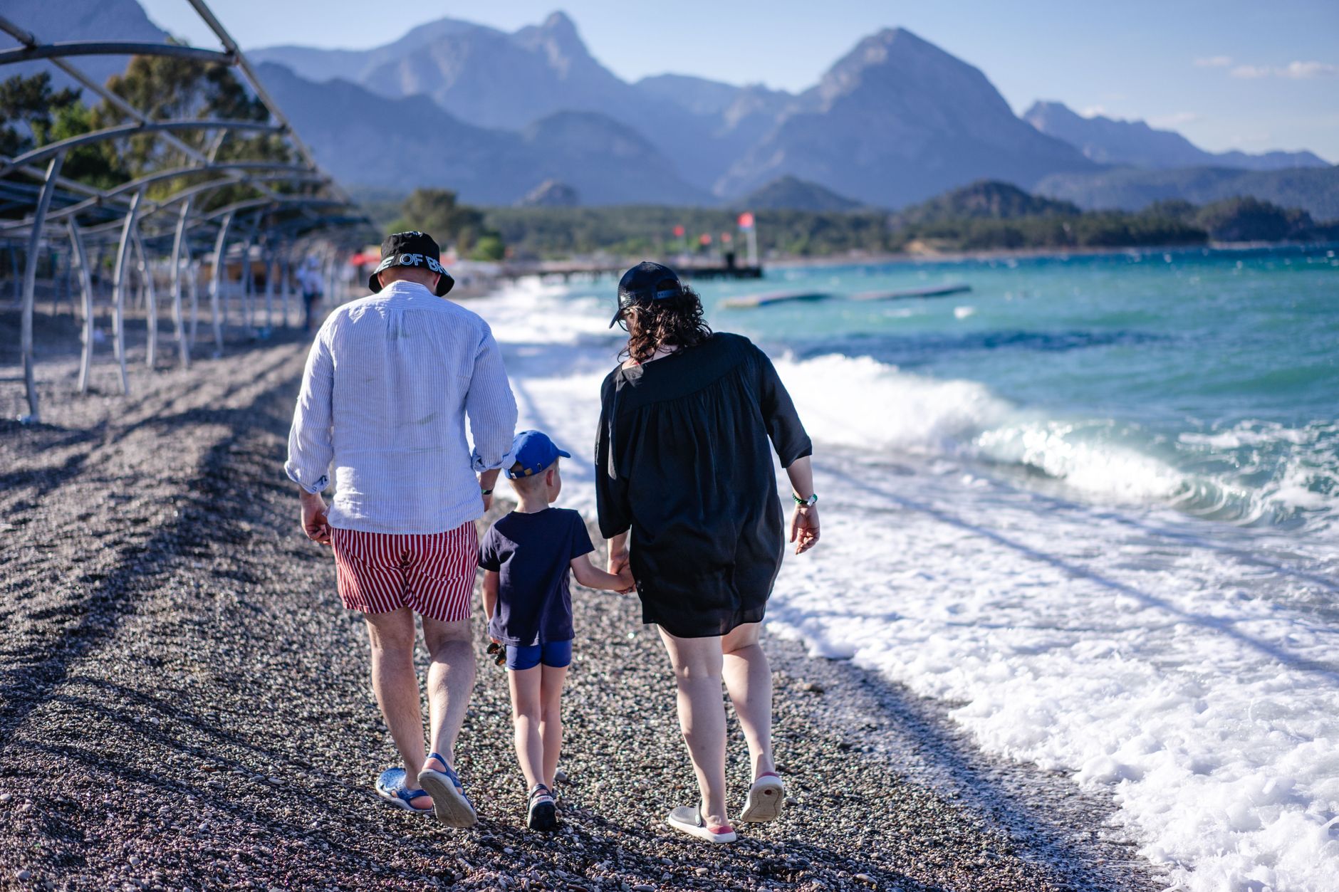 A family strolls along a pebble beach in Antalya, enjoying the Mediterranean sea.