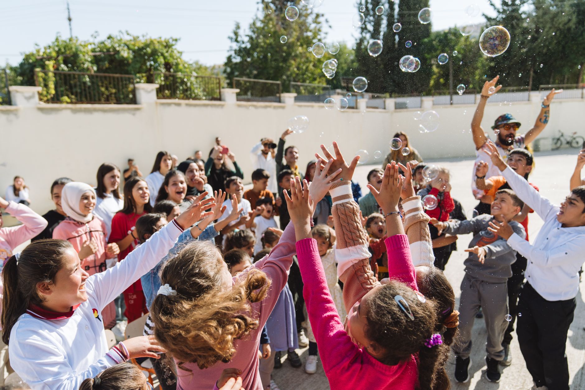 A lively group of children joyfully reaching for bubbles in a sunny park in Istanbul.