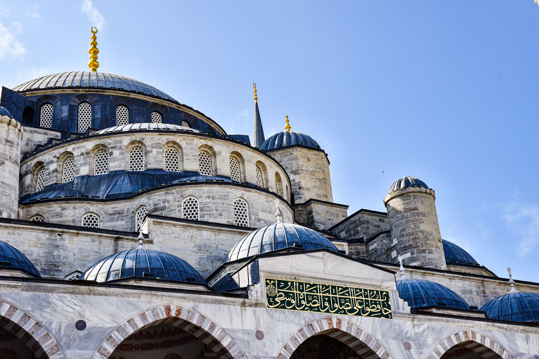 A view of domed mosque architecture in Istanbul, showcasing intricate stone work and bright blue skies.