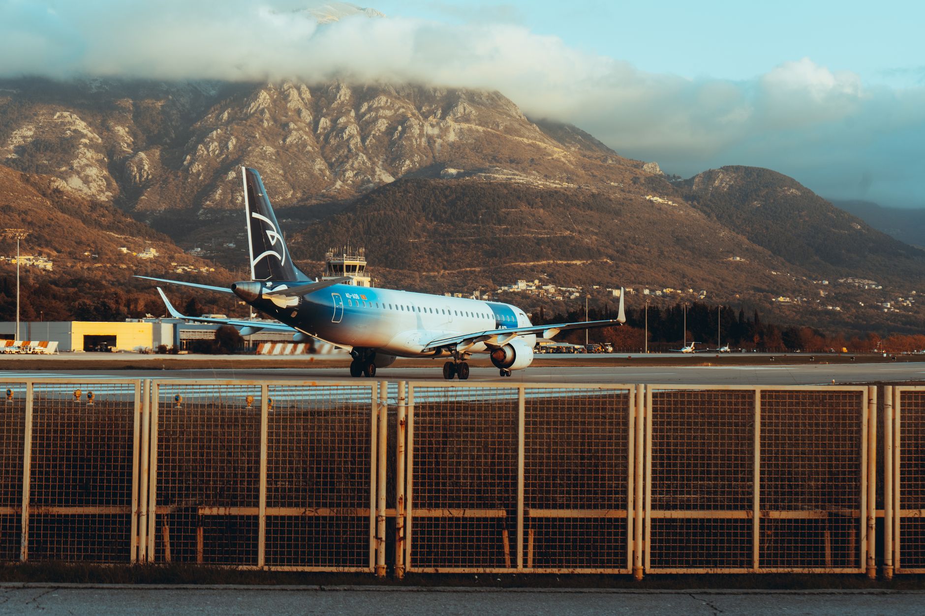 A blue airplane taxiing at an airport with mountains in the background.