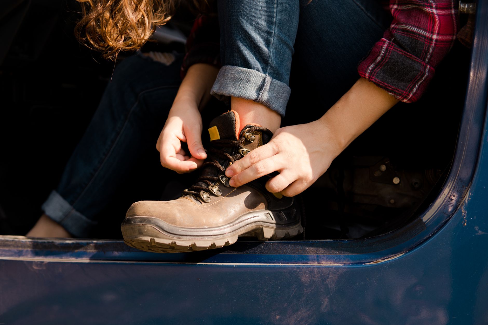 A patient is sitting in a vehicle, tying a post-operative shoe for recovery.