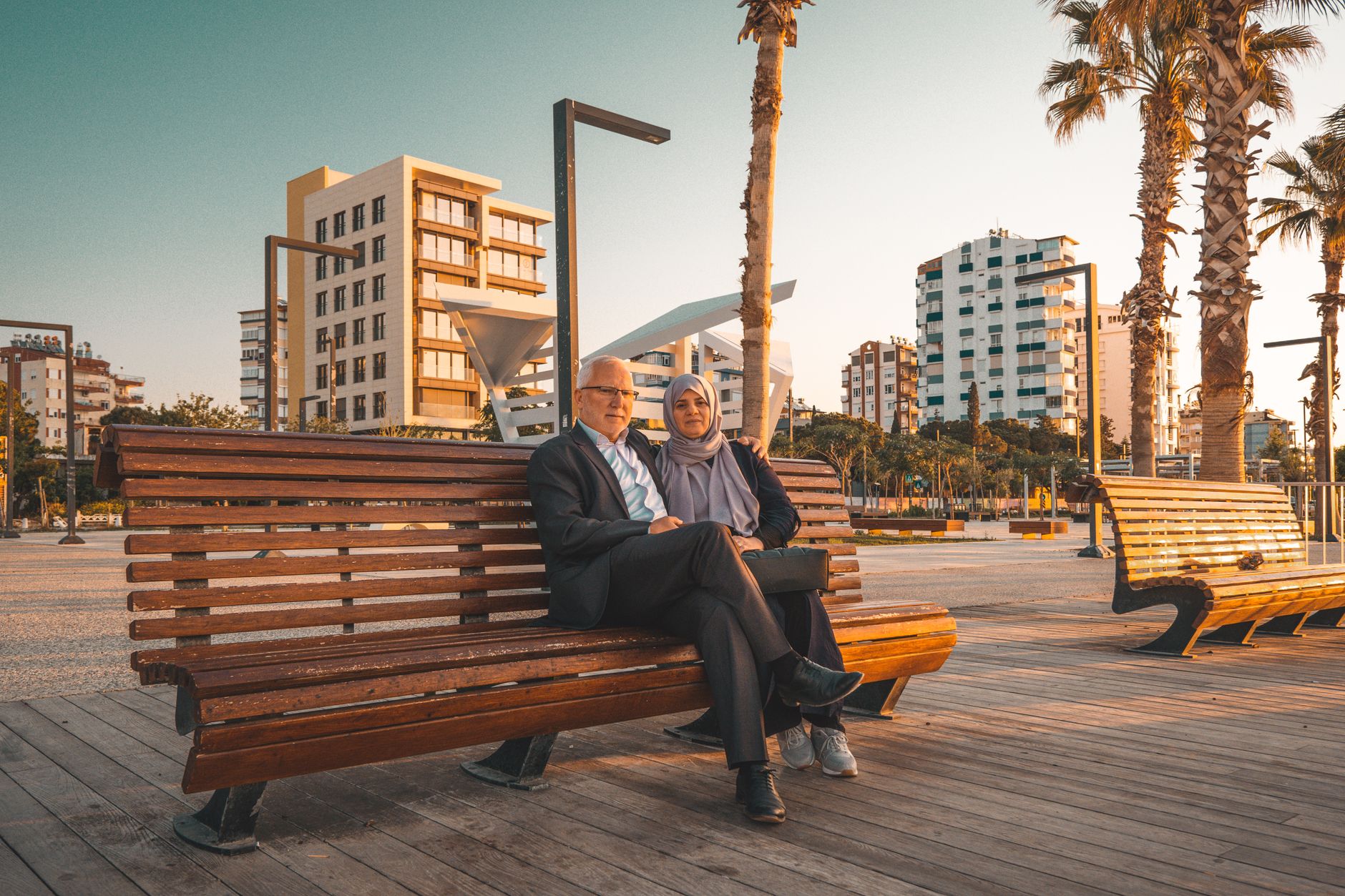 An older couple sits on a wooden bench in Antalya, enjoying the sunset.