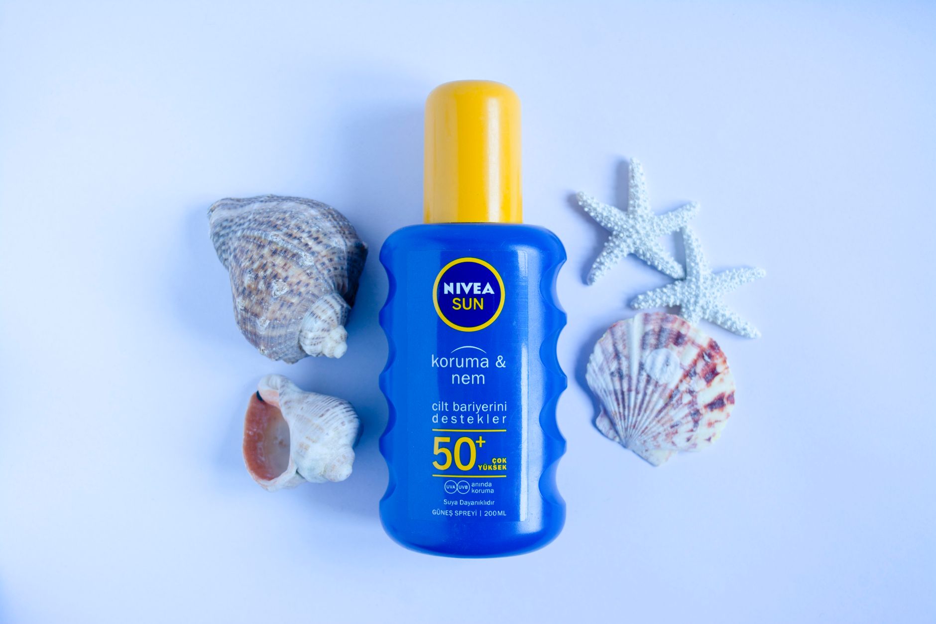 A bottle of NIVEA Sun sunscreen surrounded by seashells on a white surface.