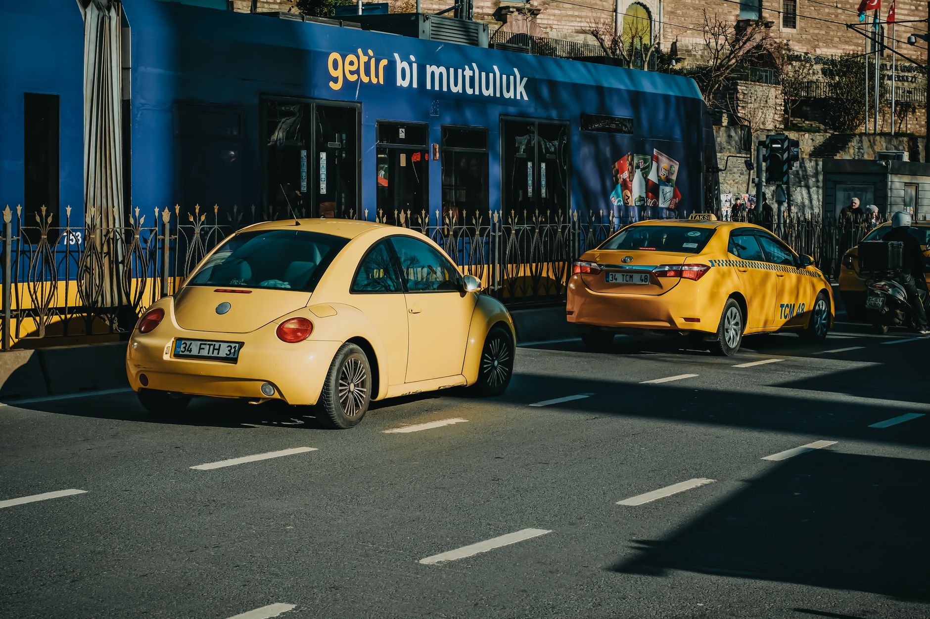 Two yellow taxis and a yellow Beetle parked on a busy street in Istanbul.