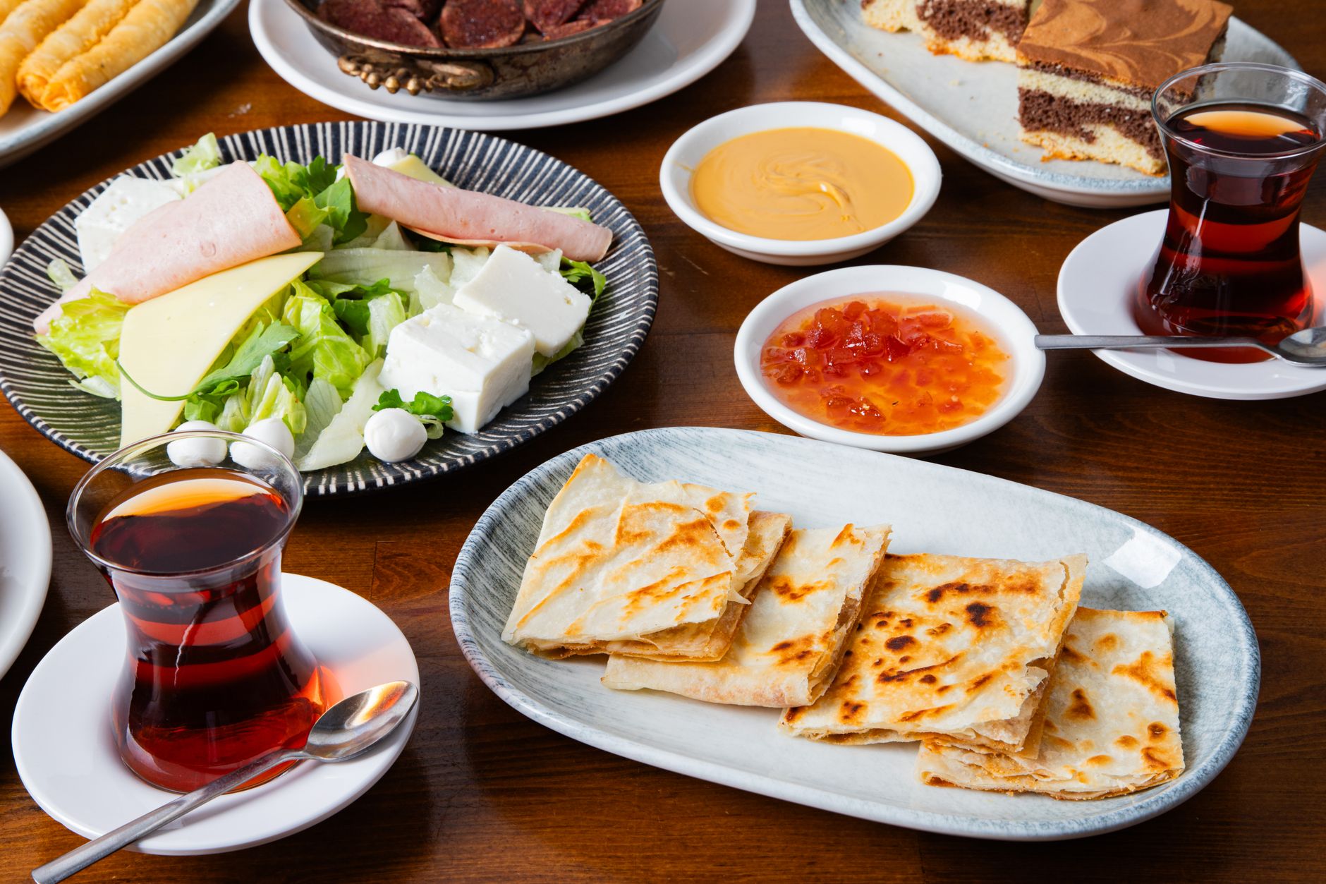 A vibrant Turkish Mediterranean spread featuring salad, cheese, tea, and flatbread.