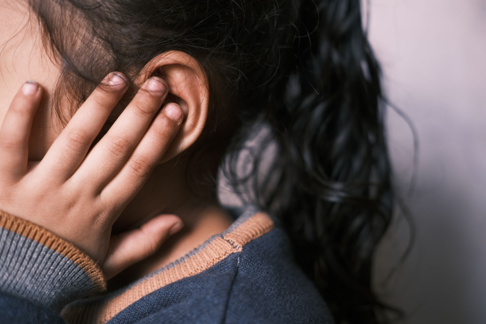 Close-up of a child's hand covering their ear, indicating a hearing test environment.