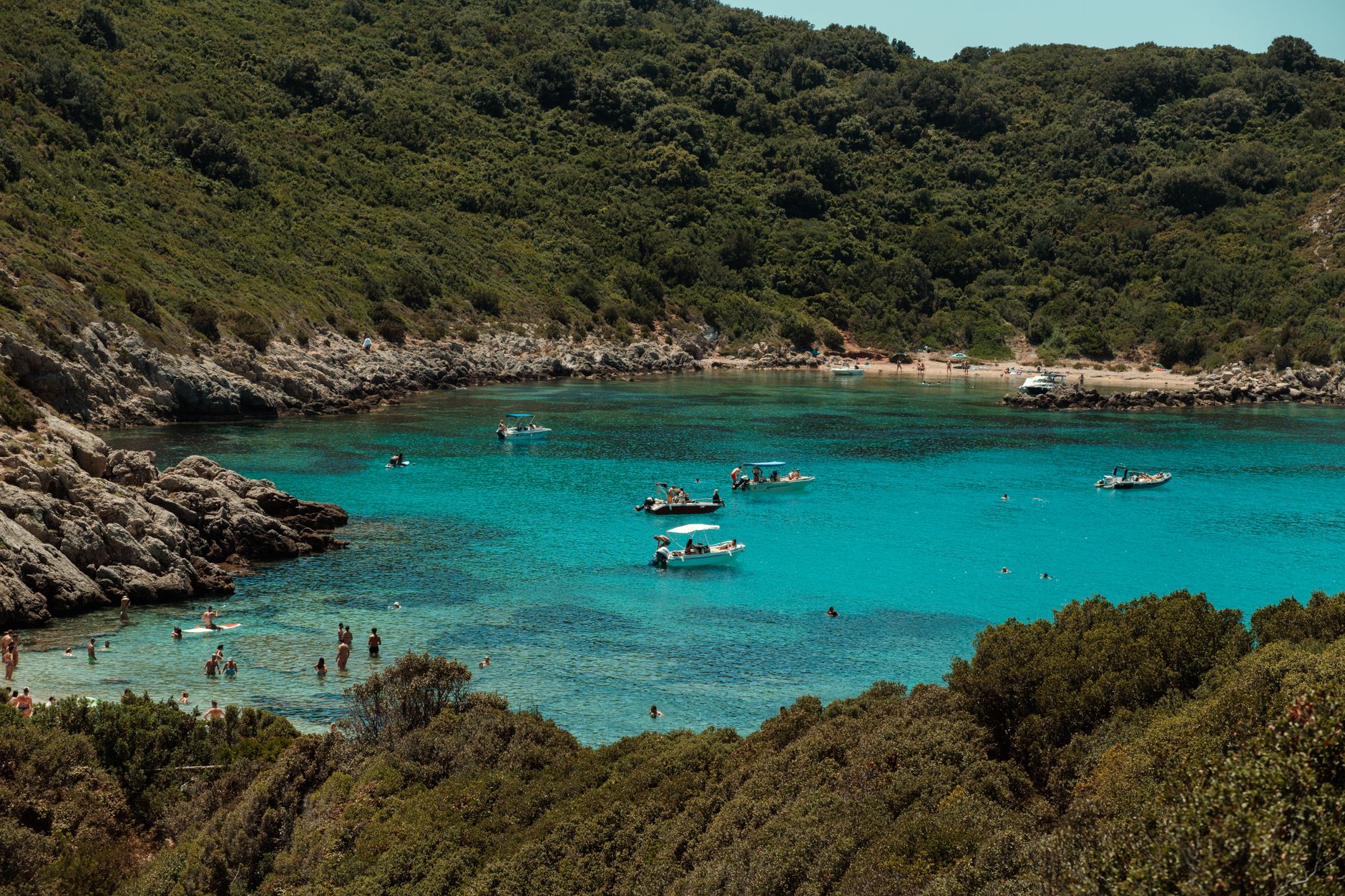 A serene bay with crystal-clear turquoise water, surrounded by lush greenery and swimmers enjoying the sun.