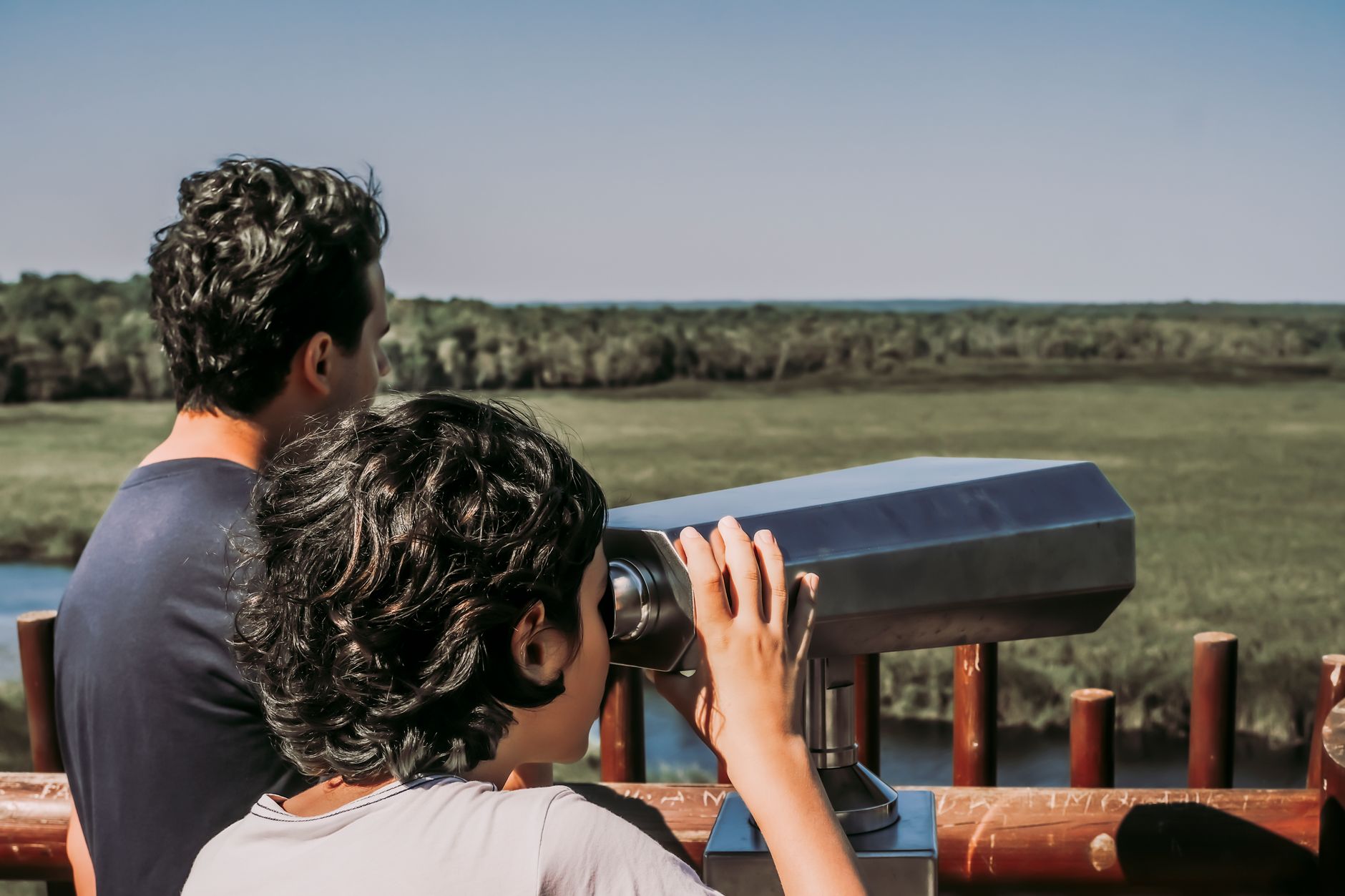 A child uses a telescope to view wildlife from a scenic overlook.
