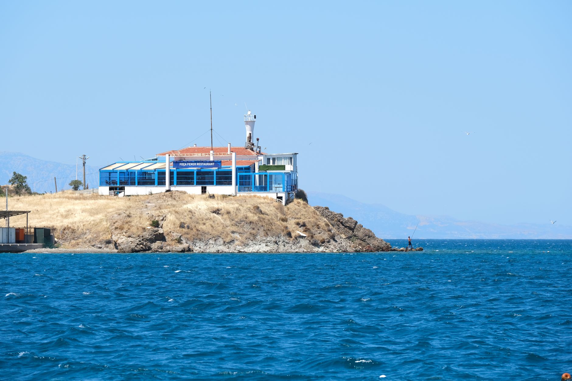 Narlıkuyu'da Foca Finer Restaurant ve kayalıklarda bir balıkçının yer aldığı huzurlu bir koy manzarası.