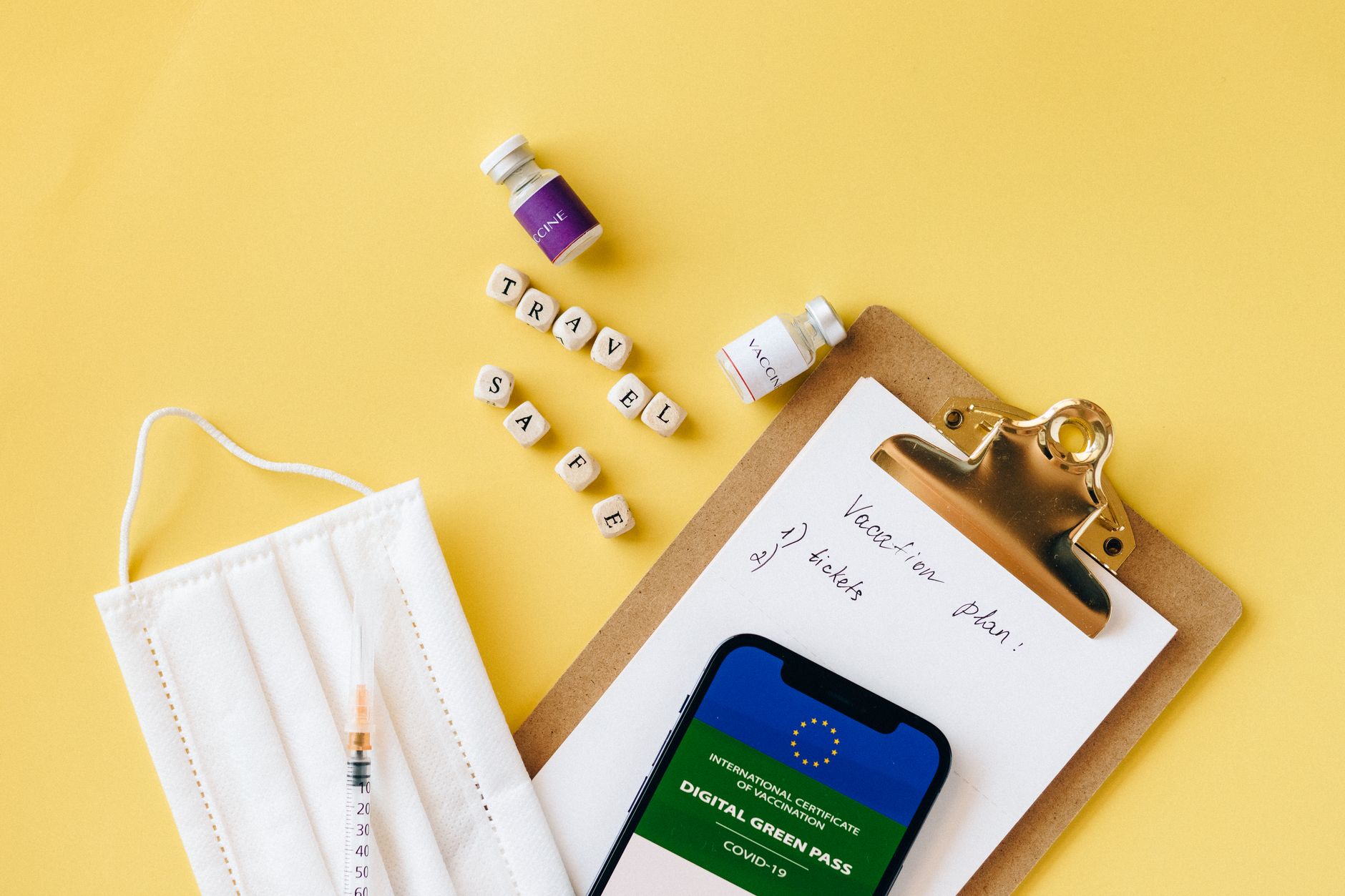 Close-up of vaccine vials, a digital health pass, a mask, and a travel checklist.