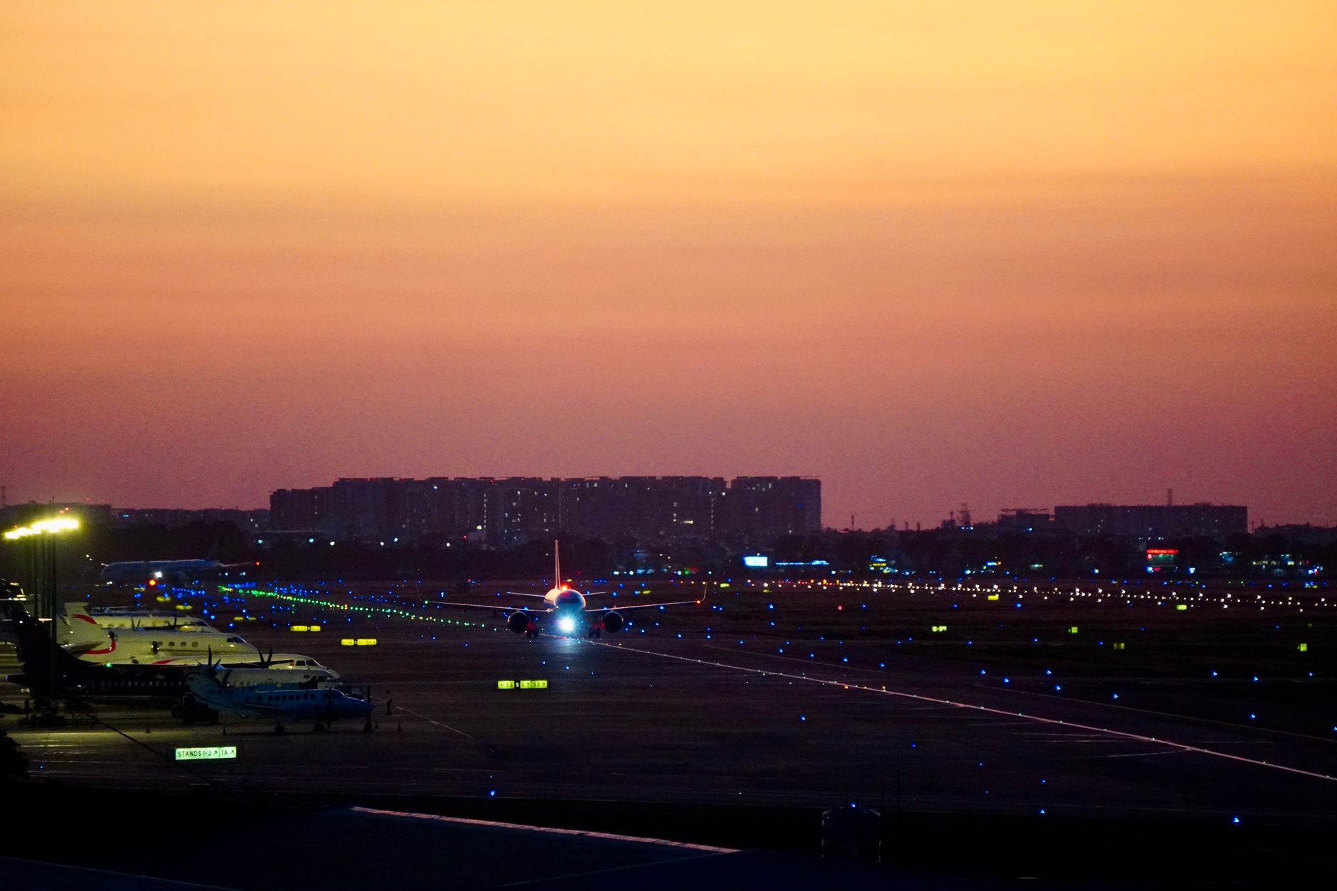 An aircraft on a runway during sunset, with illuminated lights and a colorful sky.