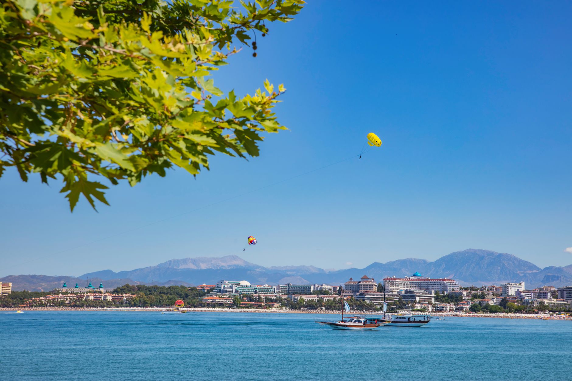 A serene view of Antalya's beach with paragliders and mountains in the background.