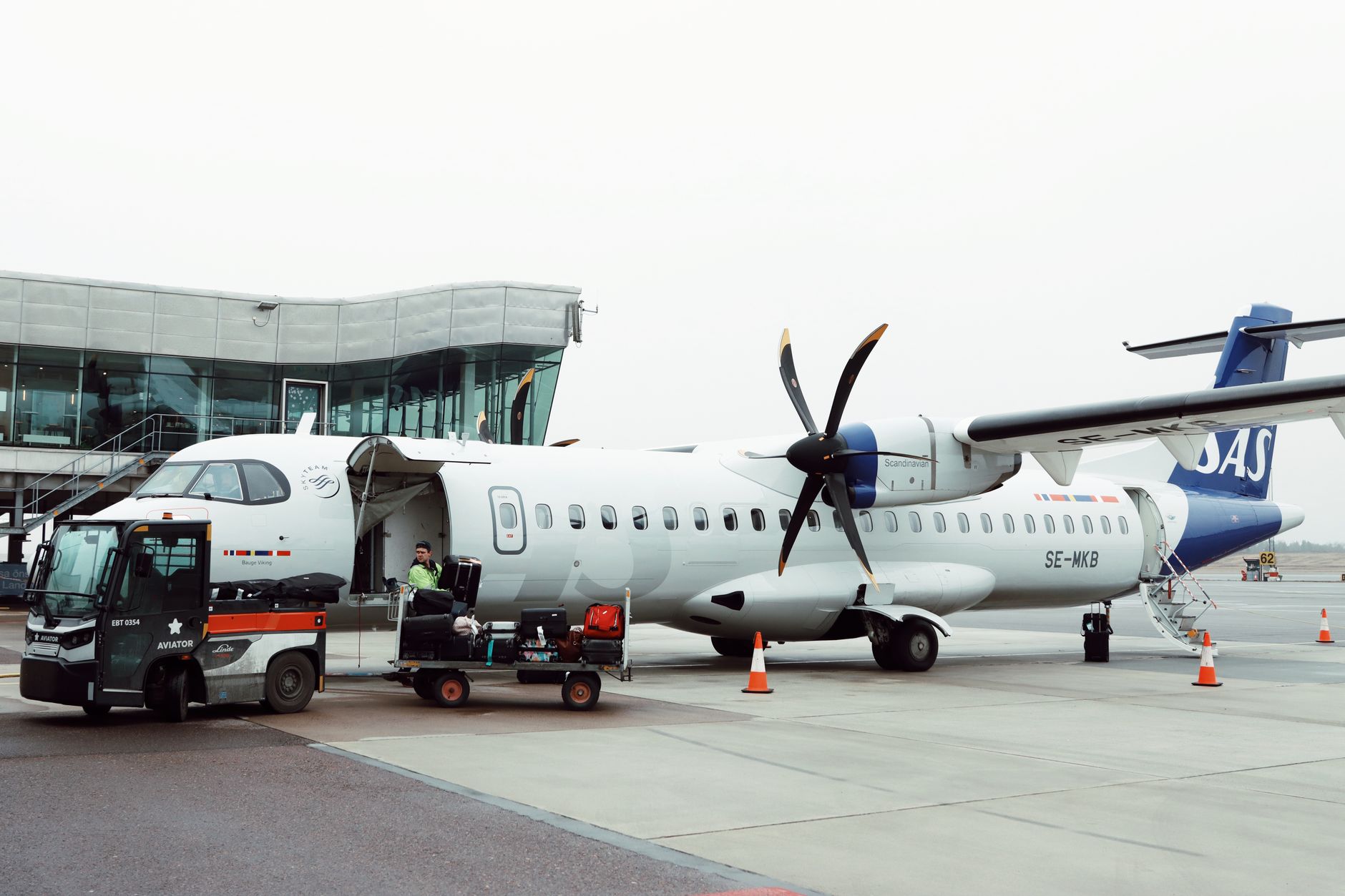 A propeller airplane being loaded with luggage at a Scandinavian airport.