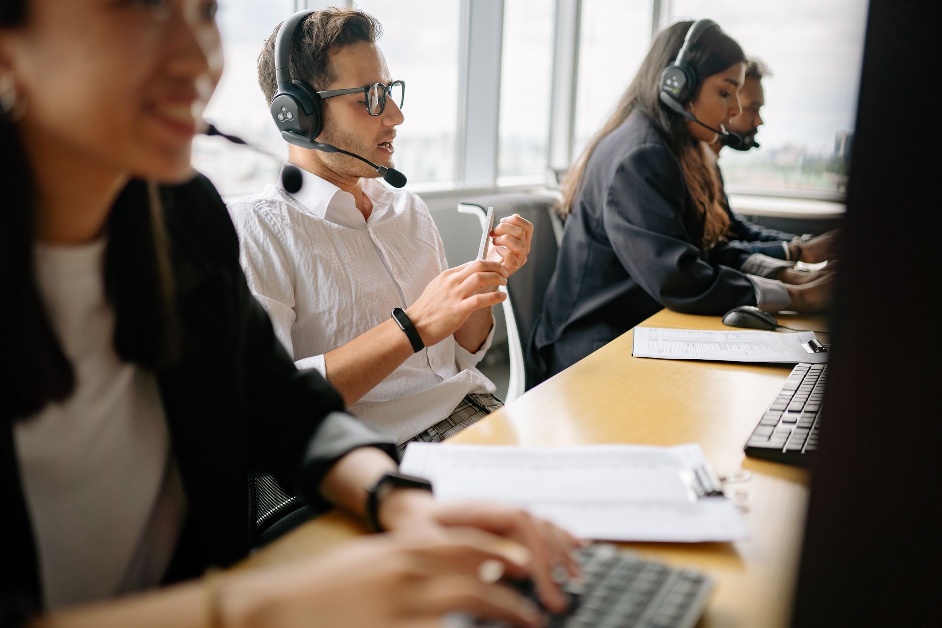 A diverse team of multilingual staff at an airport desk assisting travelers over headsets.