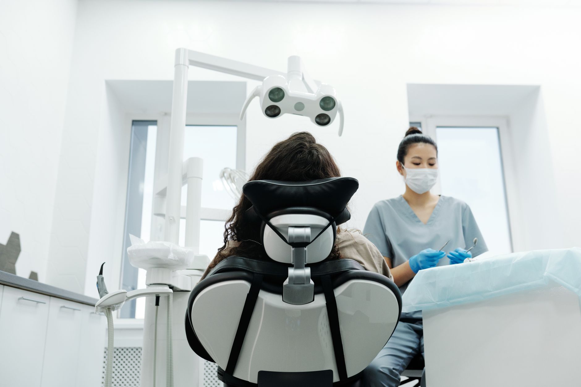 A dentist in gray scrubs treats a patient in a modern dental chair in a bright clinic.