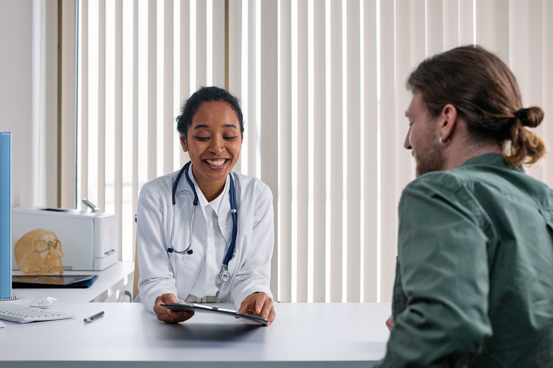 A smiling doctor shows a tablet to a patient in a bright medical office.