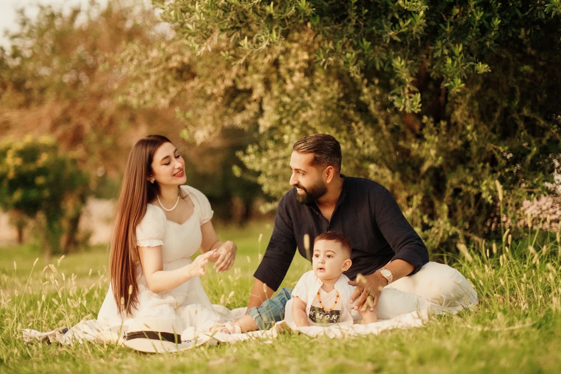 عائلة تستمتع بنزهة على منطقة عشبية بجانب جدول، ويلعبون مع طفلهم.
