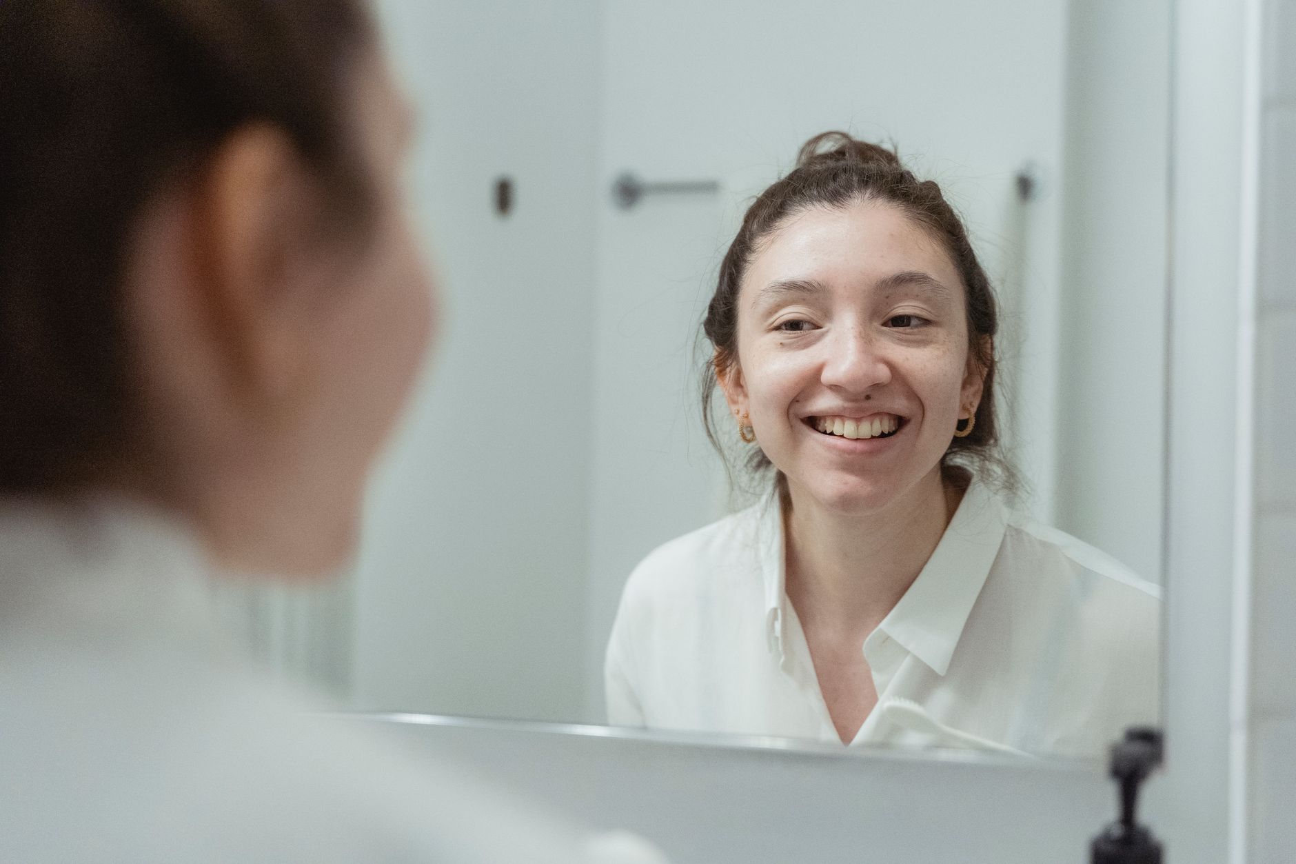 Young woman smiling at her reflection in a bathroom mirror, showcasing a refreshed look.