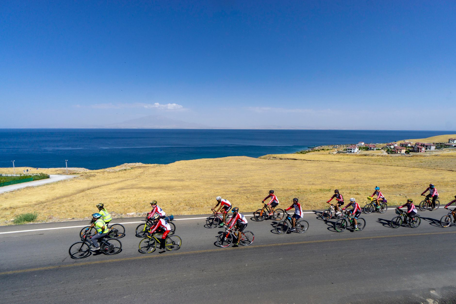 A group of cyclists on a quiet road near a serene blue lake and golden fields.
