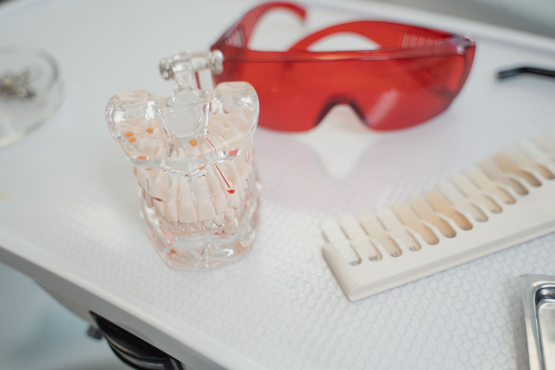 Dental model of teeth alongside red safety glasses and color matching guide.