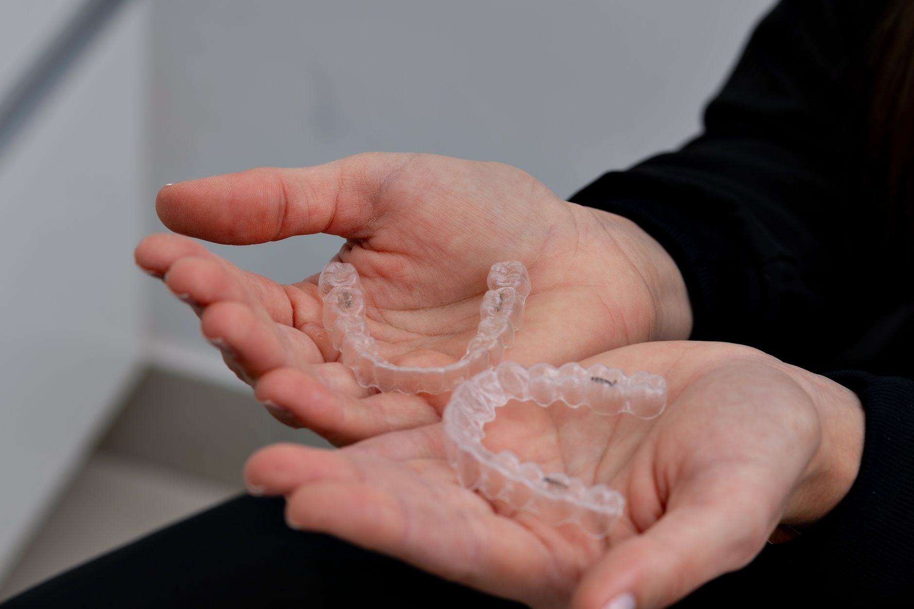 Two clear dental aligners held in hands, showcasing orthodontic treatment options.
