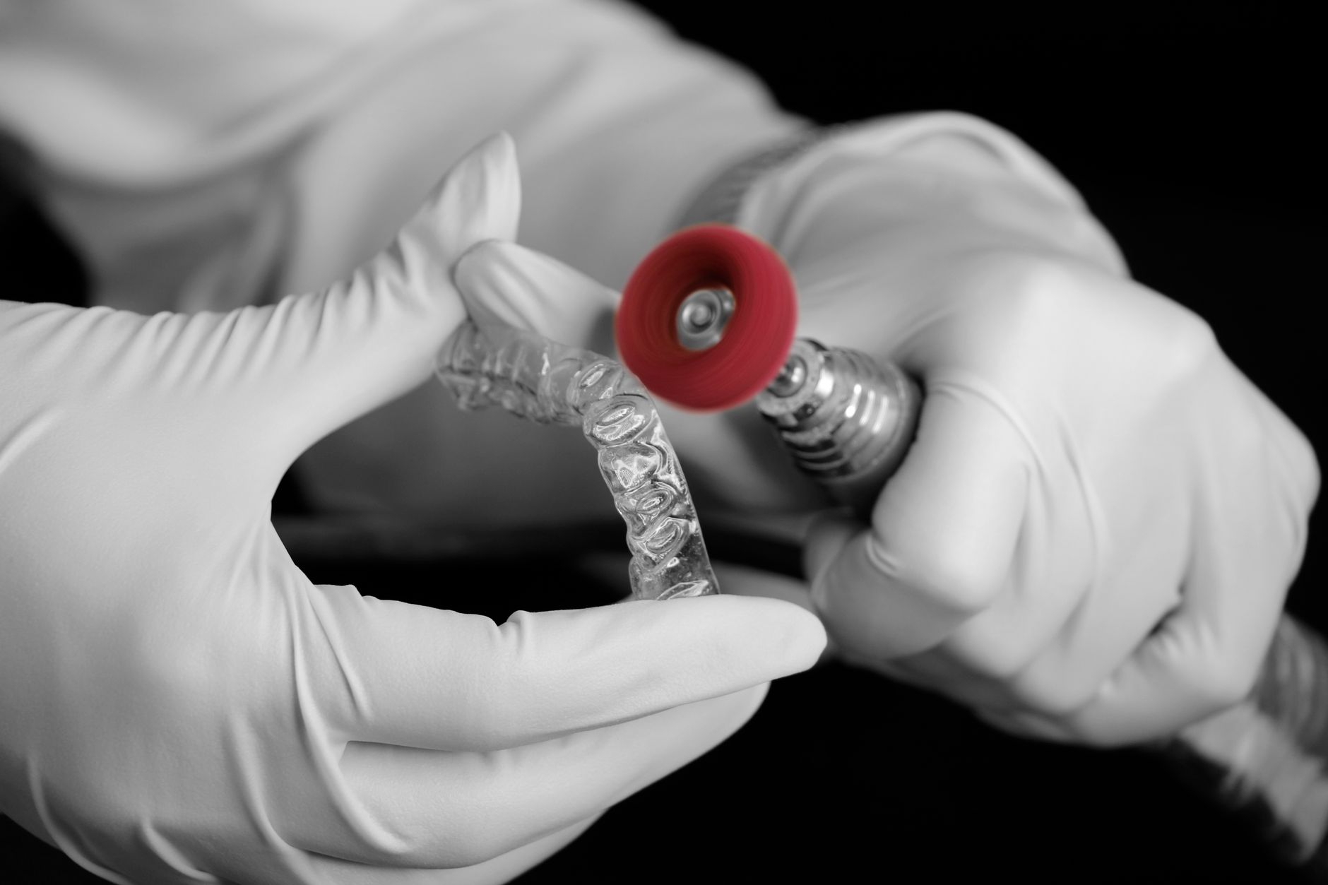 An orthodontist in gloves adjusting clear braces with a dental tool.